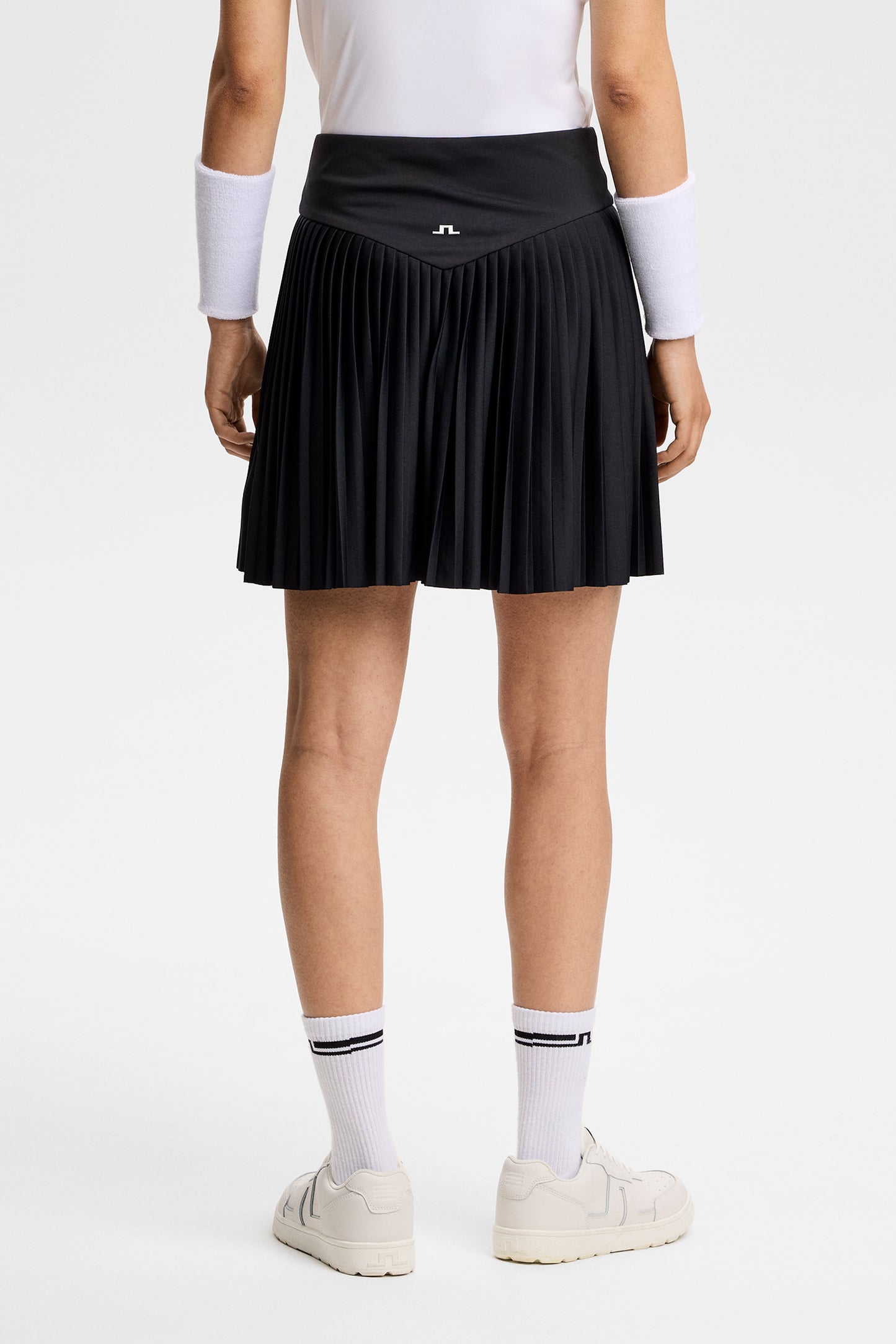 Achteraanzicht: Model draagt de zwarte Alexandra Skirt met geplooide zoom en Bridge-logo op de achterkant van de taille.