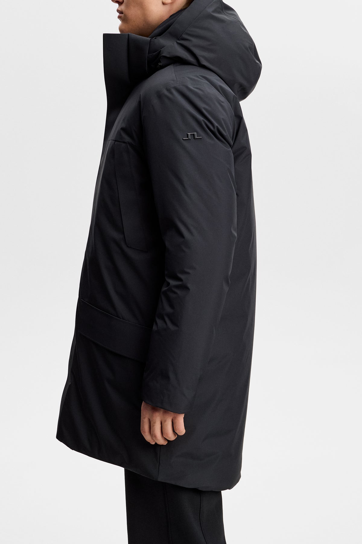 Zijaanzicht: Model draagt de zwarte Alon Down Parka met capuchon en Bridge-logo op de mouw.
