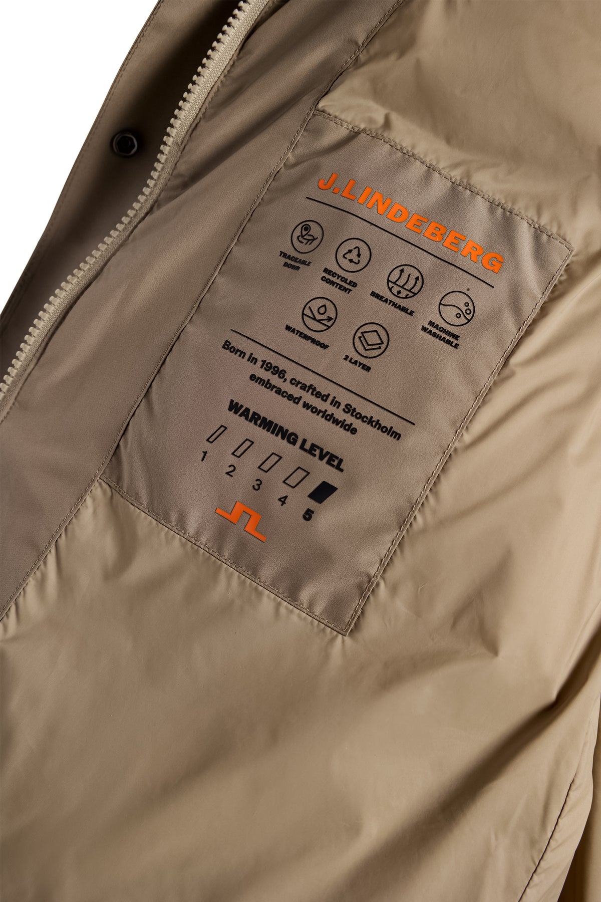 Gros plan : Lea Down Jacket en Brindle montrant la poche intérieure avec logo Bridge orange et détails techniques.