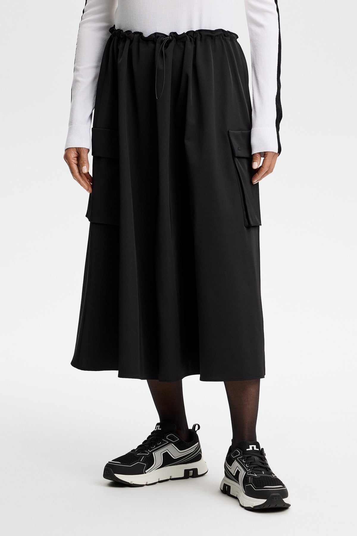 Vue de face : Essa Tech Drape Skirt noire avec cordon de serrage à la taille et poches latérales à rabat.