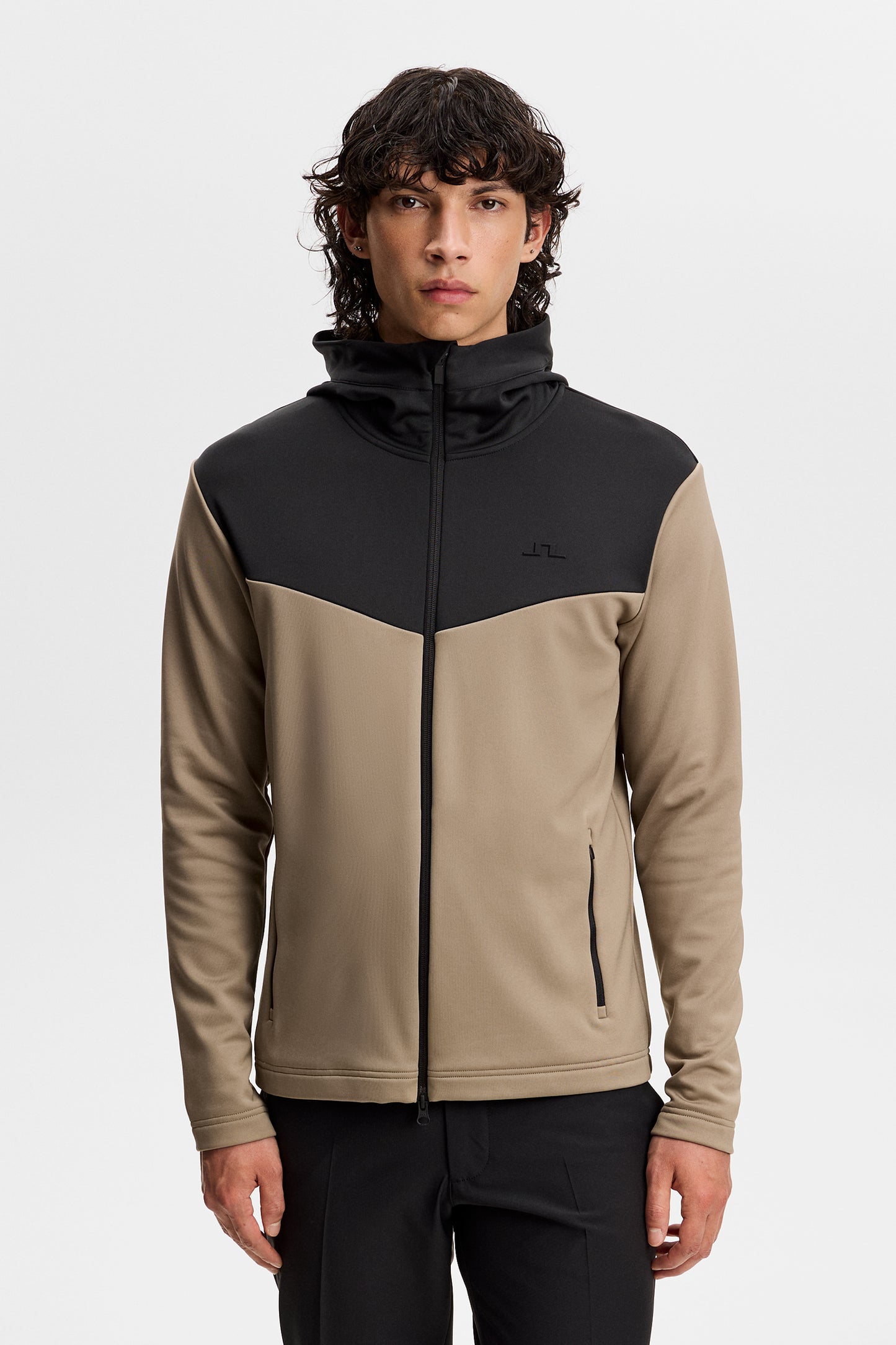 Model wearing the Maclean Zip Hood in black and beige, front view with color-block design and small Bridge logo.