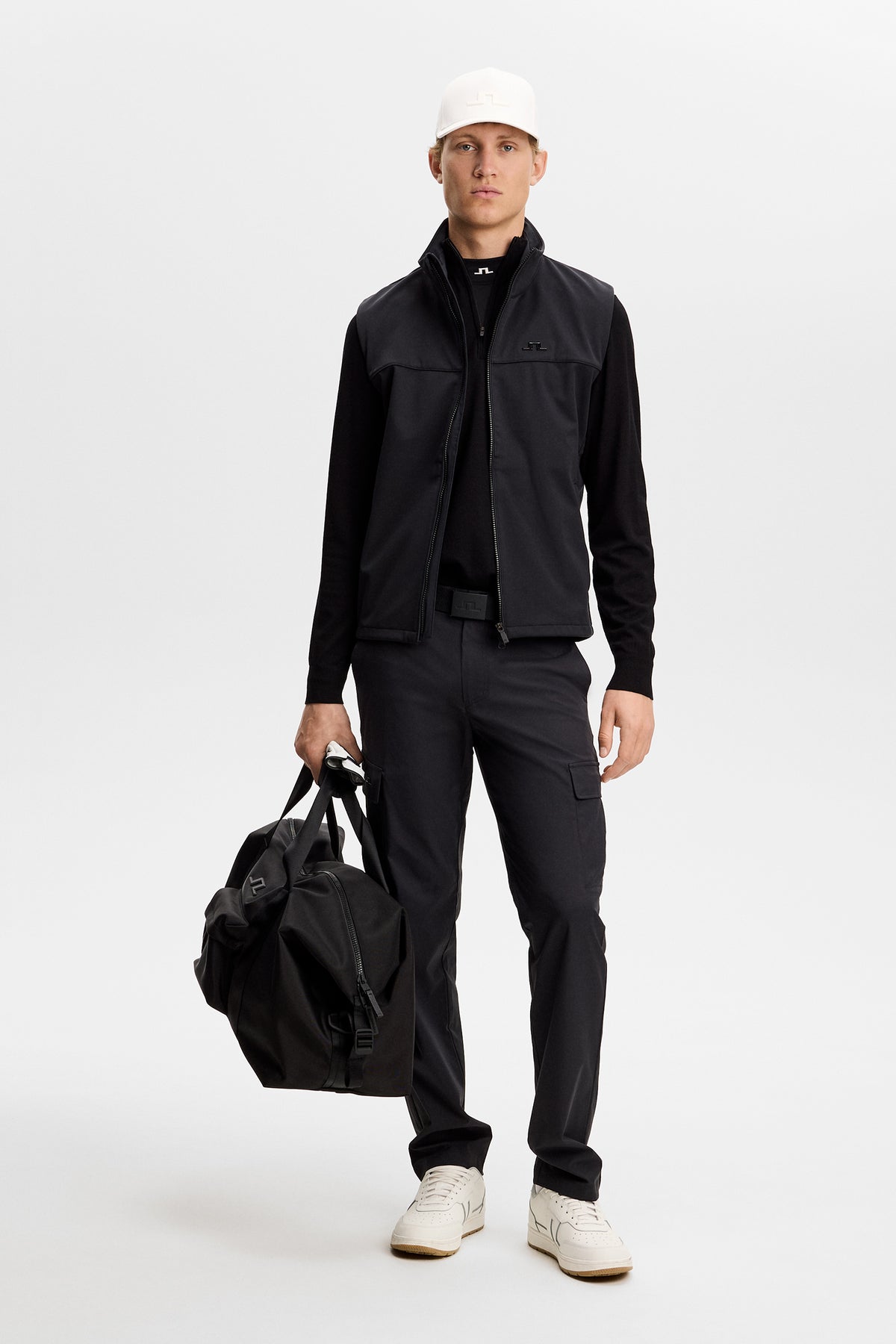 Vorderansicht: Schwarzer Kendrick Knitted Zip Sweater am Model, unter einer Weste mit Cargohose im Studio.