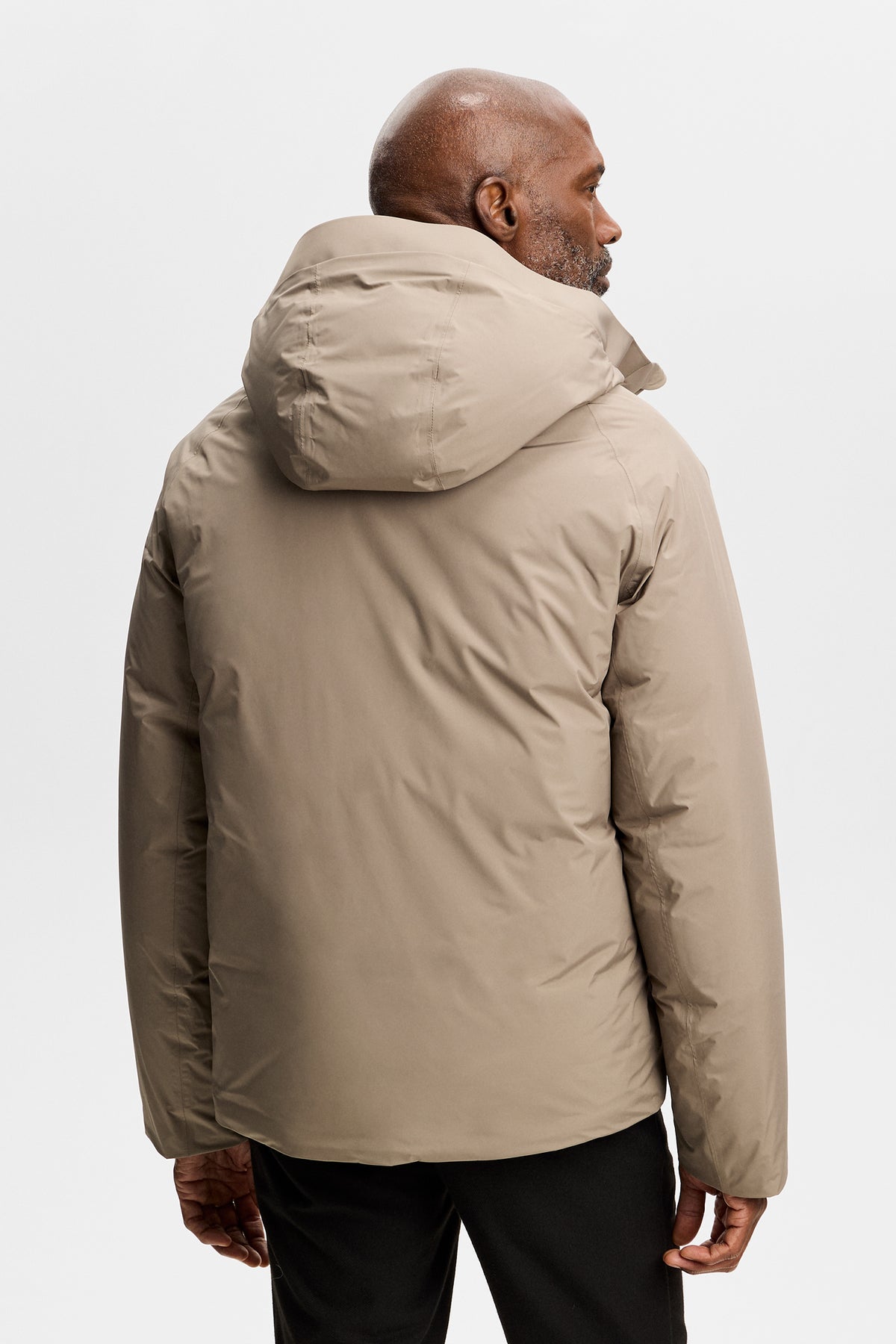 Achteraanzicht: Model draagt de Alvin Down Jacket in Brindle met capuchon en een zwarte broek.