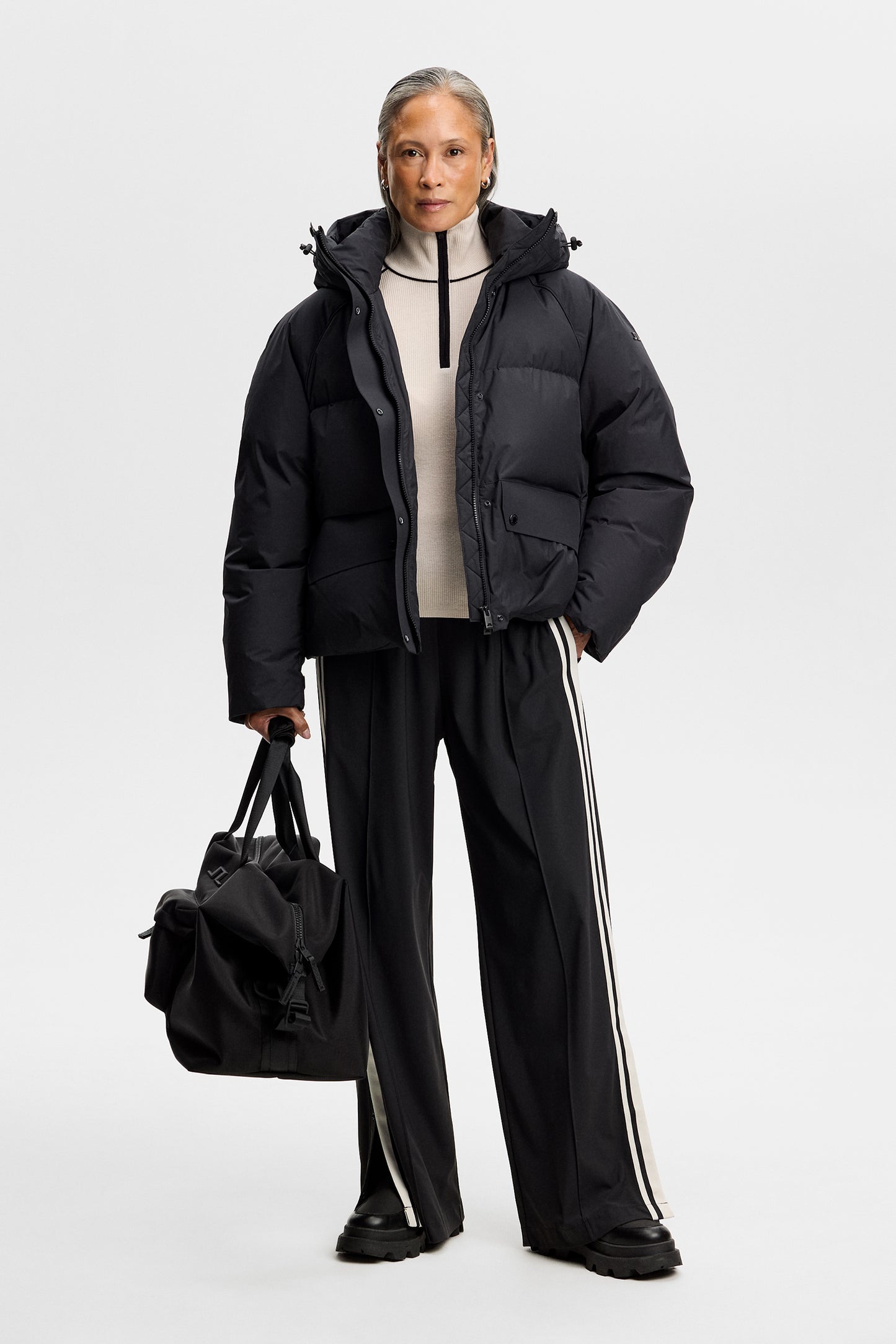 Vooraanzicht: Model draagt de zwarte Lea Down Jacket open over een lichte trui met zwarte broek en tas.