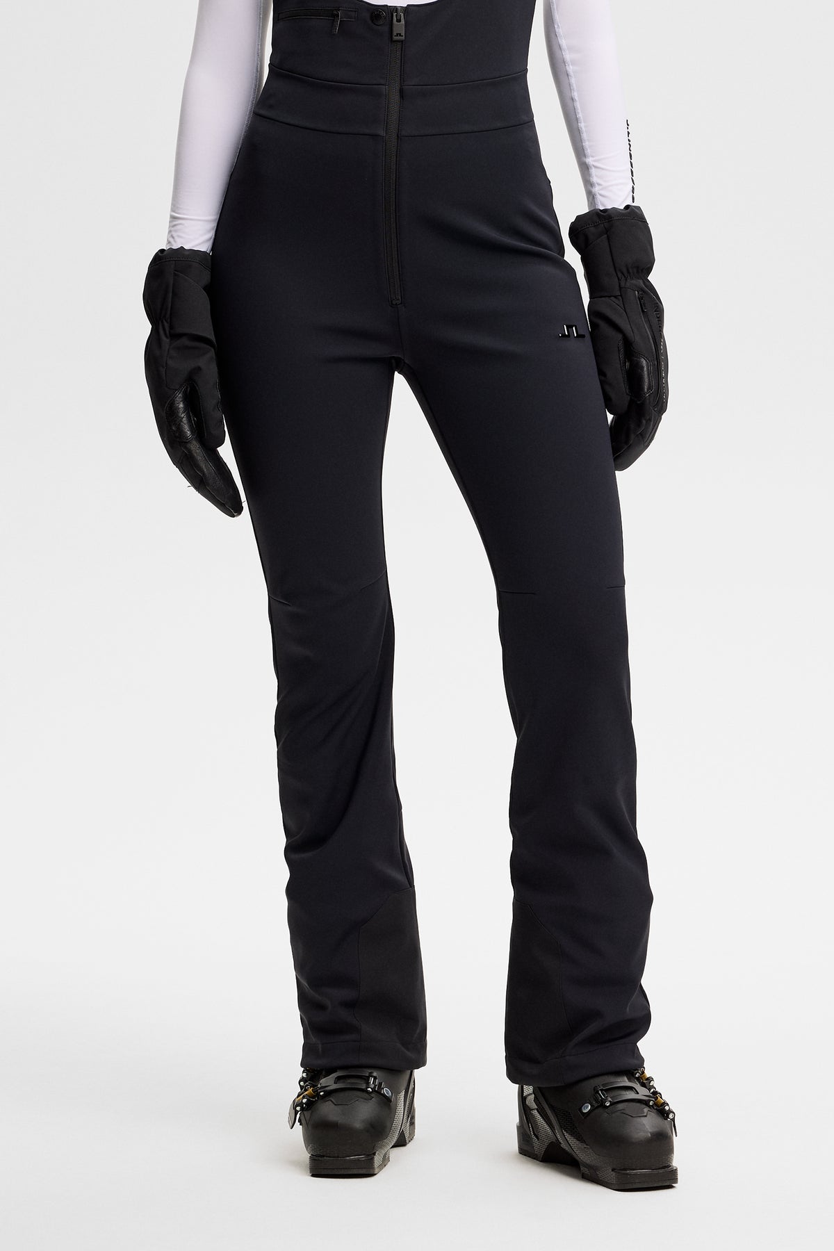 Vooraanzicht: Model draagt de zwarte Aviana Softshell Bib Pant met ritssluiting en Bridge-logo op het been.