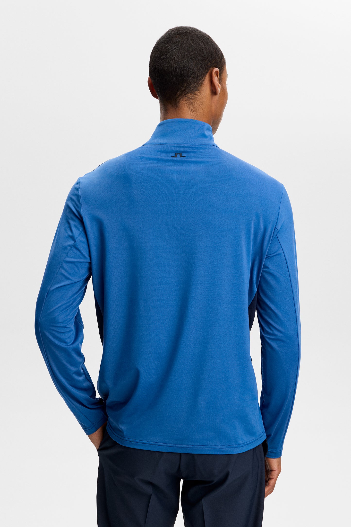 Achteraanzicht: Model draagt de blauwe Finn Quarter Zip Mid Layer met lange mouwen en Bridge-logo in de nek.