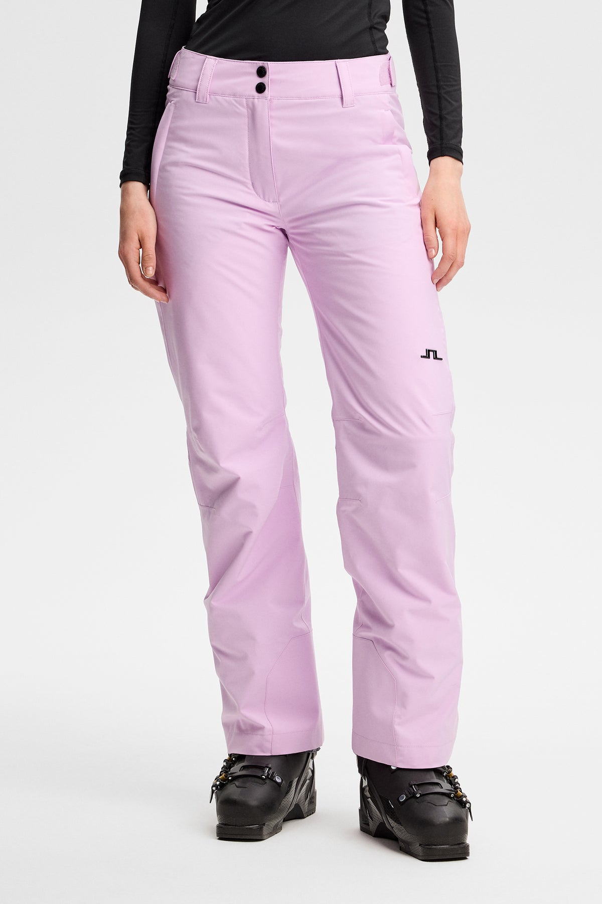 Vorderansicht: Moeva Pant in Orchid Bouquet mit Bridge-Logo am linken Bein, kombiniert mit Skischuhen.