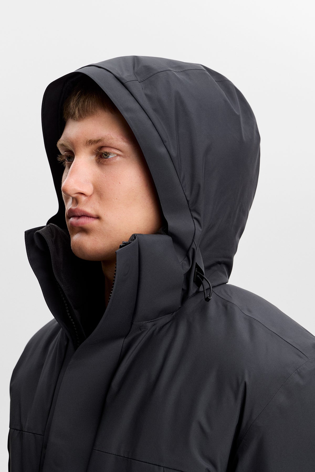 Close-up zijkant: Model draagt de zwarte Alon Down Parka met hoge kraag en capuchon.