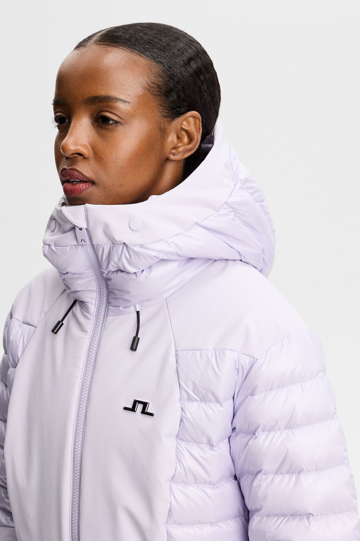 Nærbillede: Maelle Down Jacket i Purple Heather med hætte, høj krave og Bridge-logo på brystet.