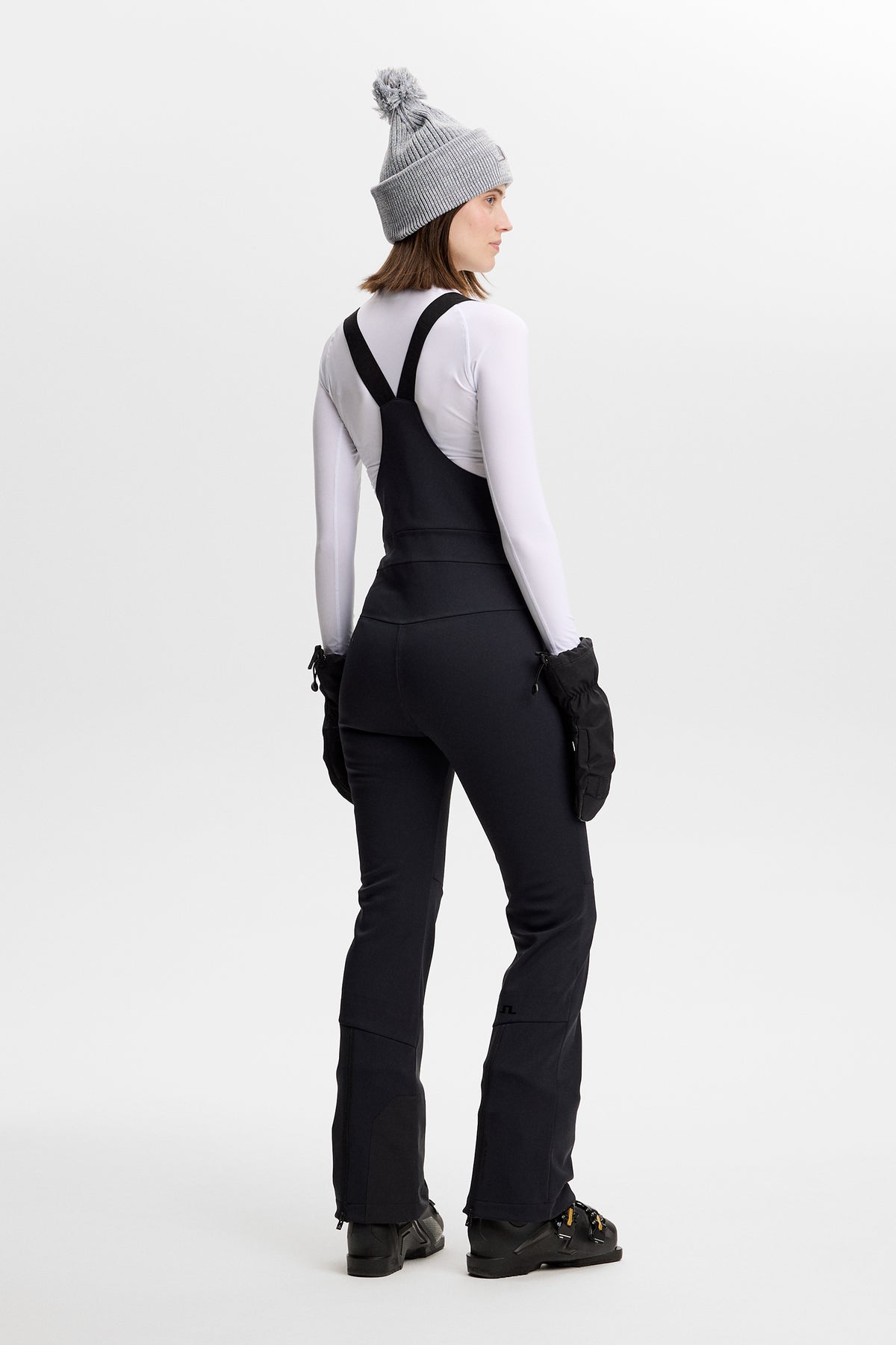 Achteraanzicht: Model draagt de Aviana Softshell Bib Pant in Black met bretels over een witte top.