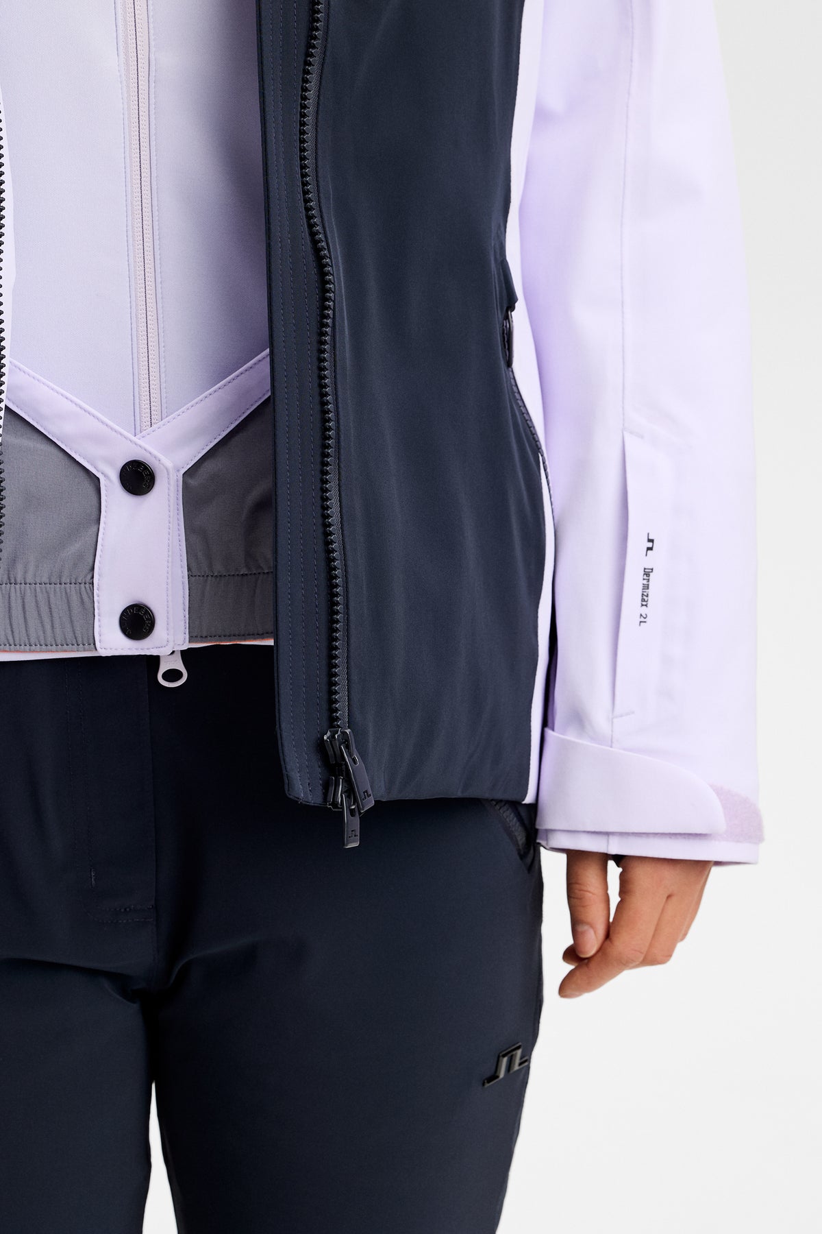 Detailansicht: Soleil Down Jacket in Purple Heather mit geöffnetem Reißverschluss, Schneefang und Ärmeltasche mit Logo.