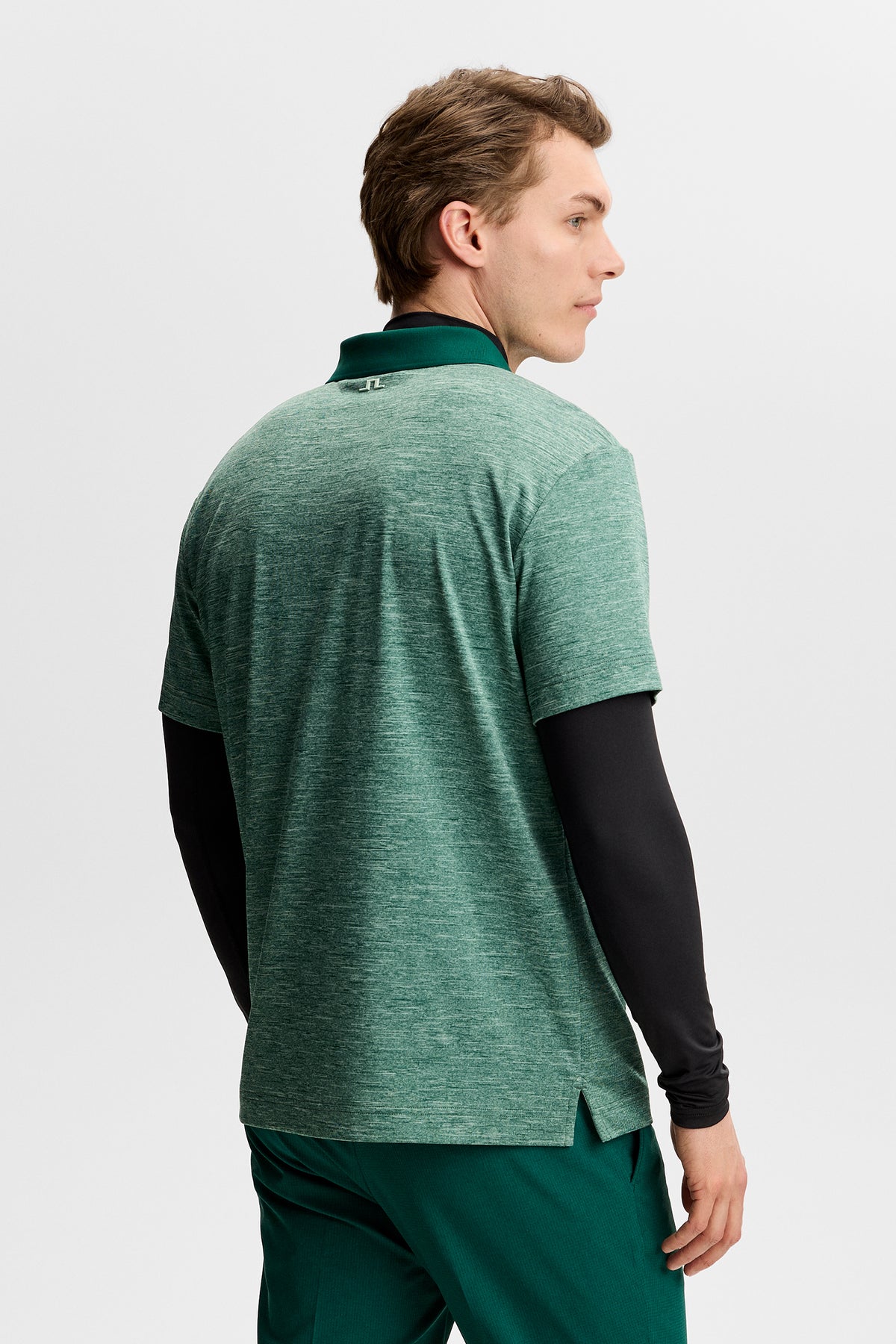 Rocky Polo in green melange, back view showing the small Bridge logo on the collar, layered over a black long-sleeve.