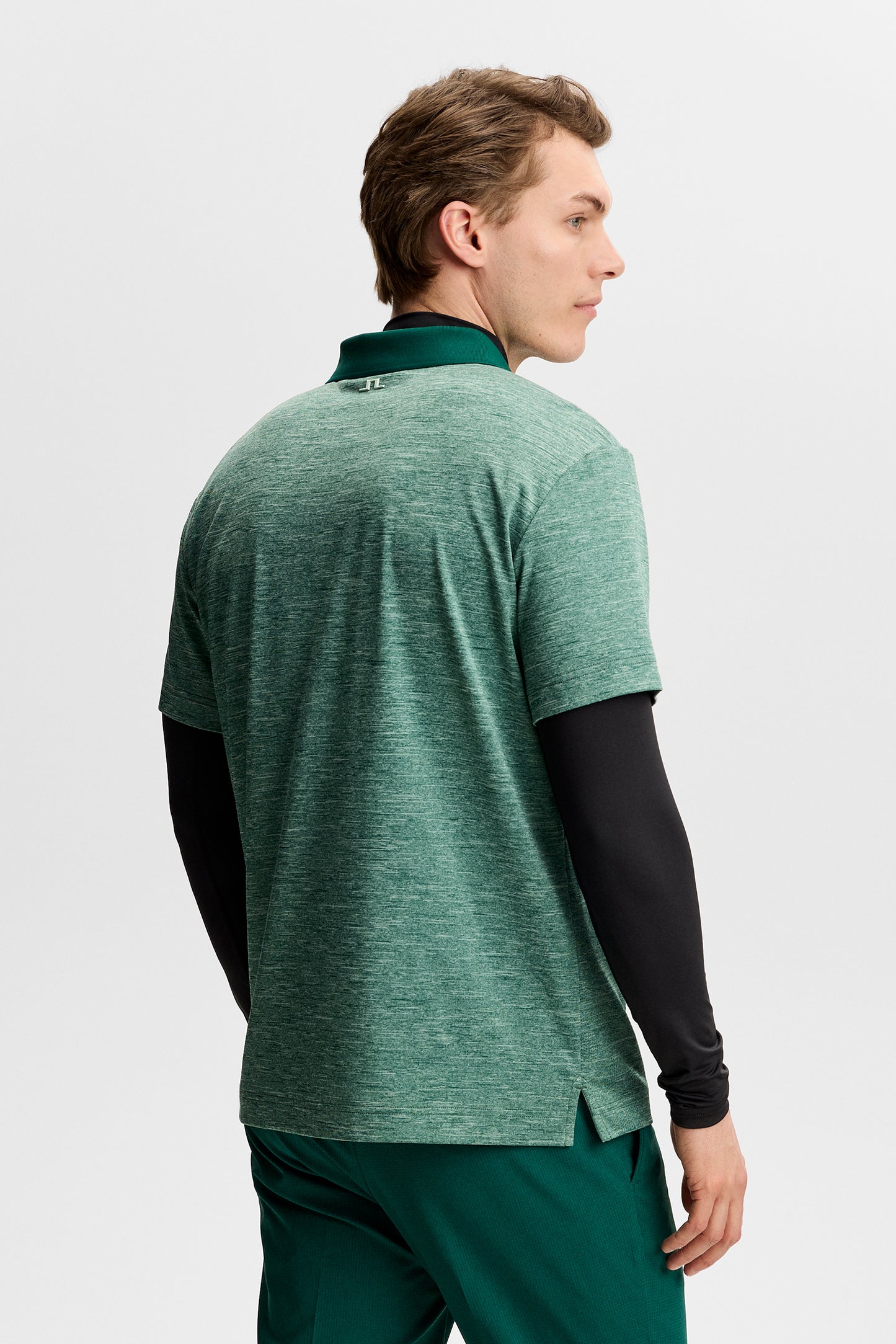 Rocky Polo in green melange, back view showing the small Bridge logo on the collar, layered over a black long-sleeve.