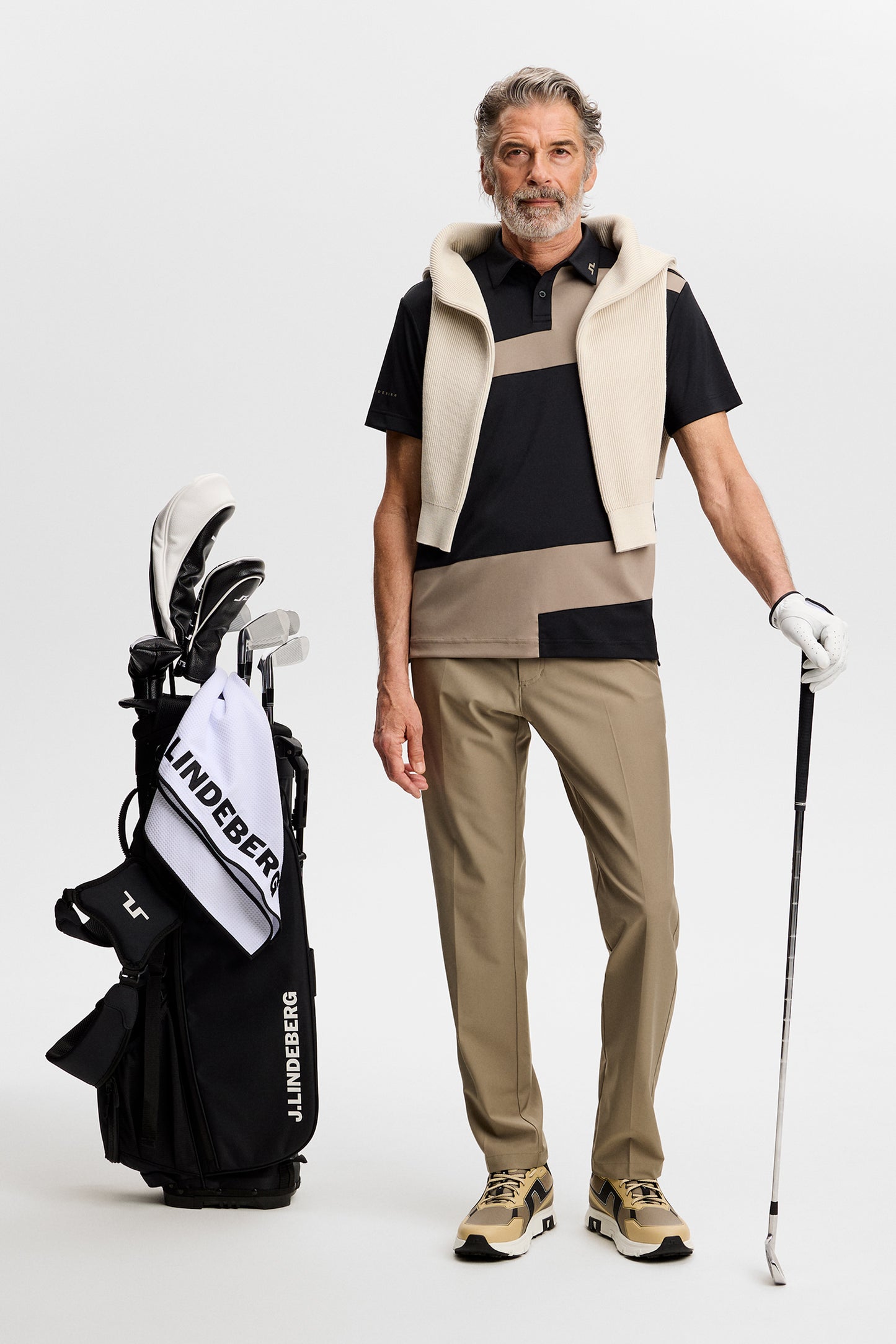 Model wearing the black and beige Sidd Polo with contrast front panels in a studio, holding a golf club.