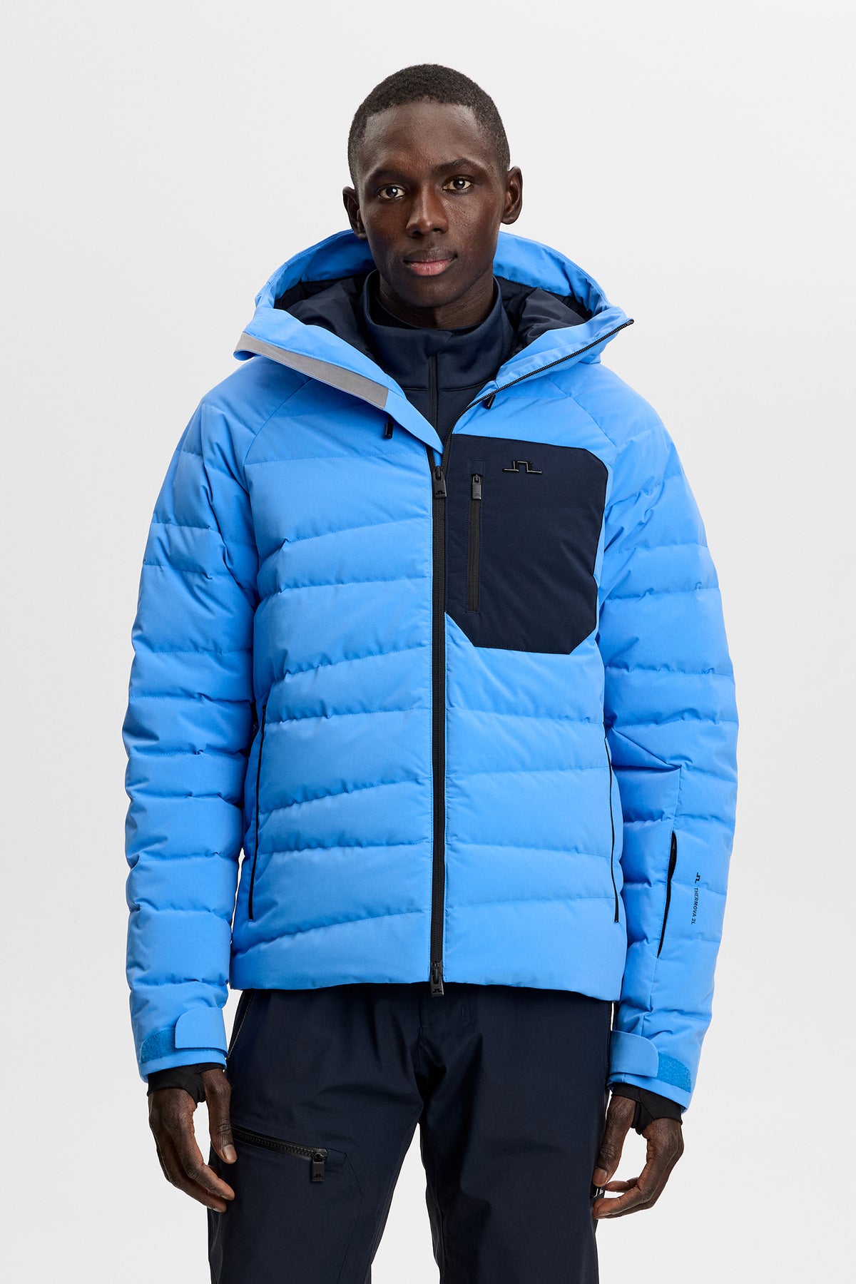 Thornton Down Jacket in Sonic Blue, front view with hood, quilted panels, and contrast chest pocket.