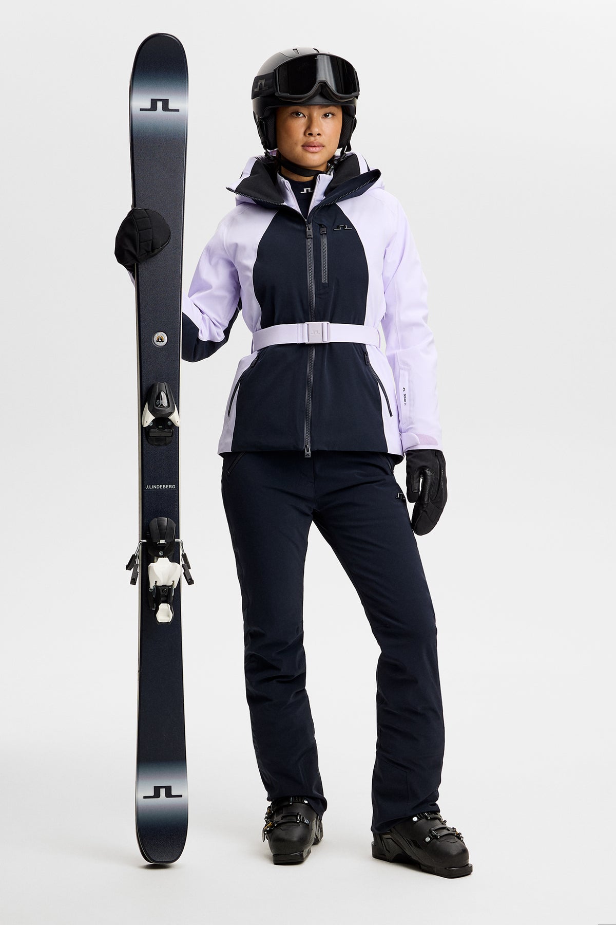 Vorderansicht: Soleil Down Jacket in Flieder und Navy mit Gürtel, getragen von einem Model mit Ski und Helm.