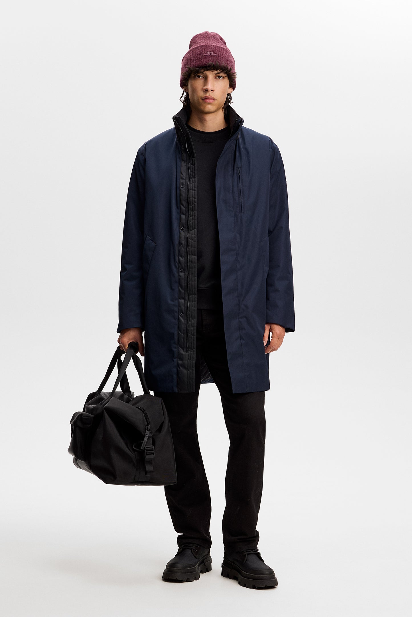 Model wearing the JL Navy Harold Padded Jacket open over a black outfit, holding a black bag in a studio setting.