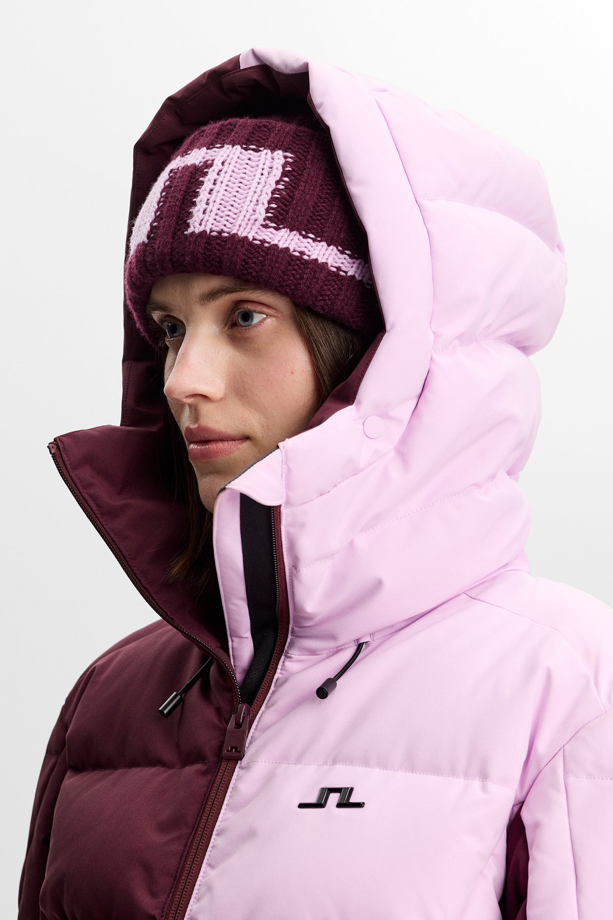 Detailansicht: Nerina Blocked Down Jacket in Winetasting mit Kapuze, hohem Kragen und Bridge-Logo auf der Brust.