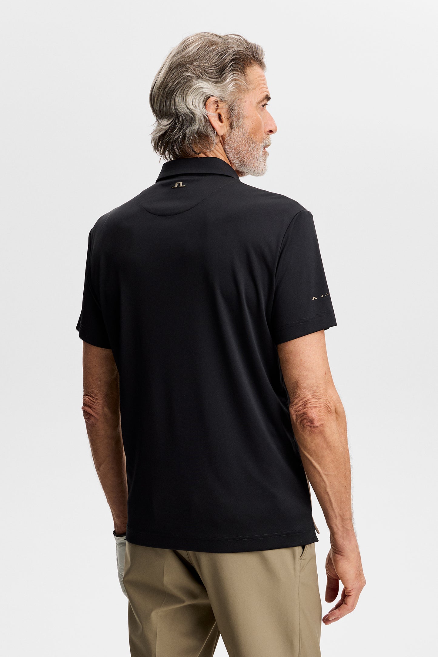 Back view: Model wearing the black Sidd Polo, showing short sleeves and a small Bridge logo at the neck.
