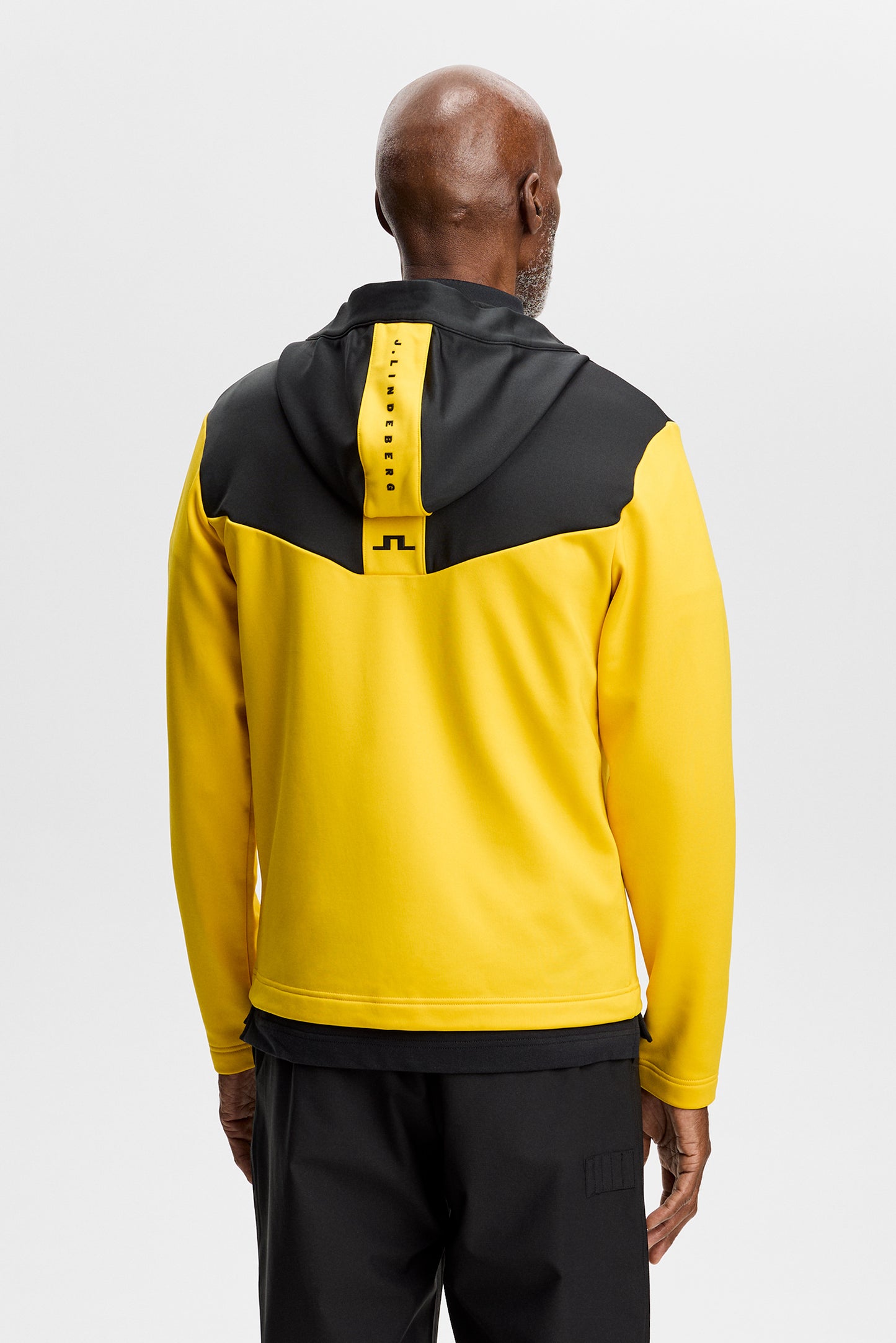 Set bagfra: Gul Maclean Zip Hood med sort kontrastpanel over skuldrene og Bridge-logo på ryggen.