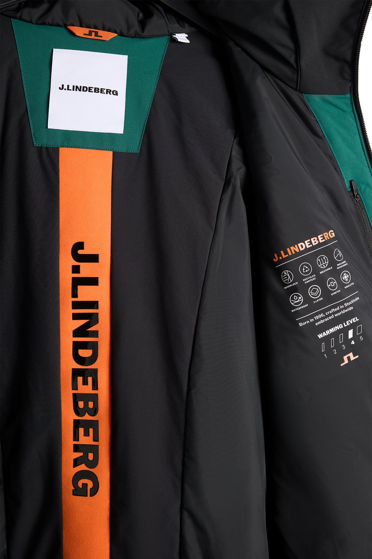 Nærbillede: Indersiden af Carrington Blocked Jacket med sort for, orange J.LINDEBERG-stribe og trykte ikoner.