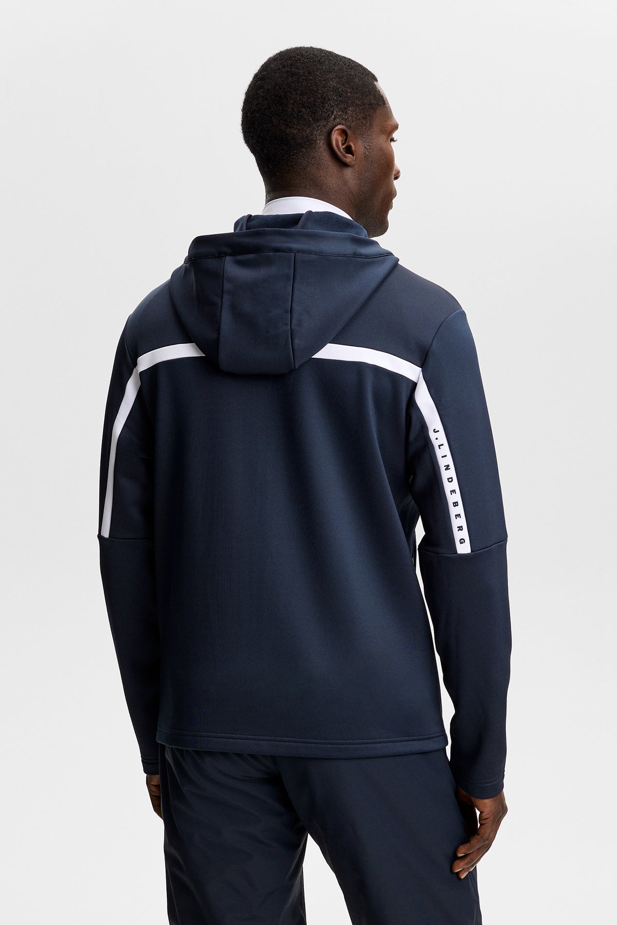 Sett bakfra: Sharpe Full Zip Hood i JL Navy på modell, med hette og hvit kontraststripe over rygg og ermer.