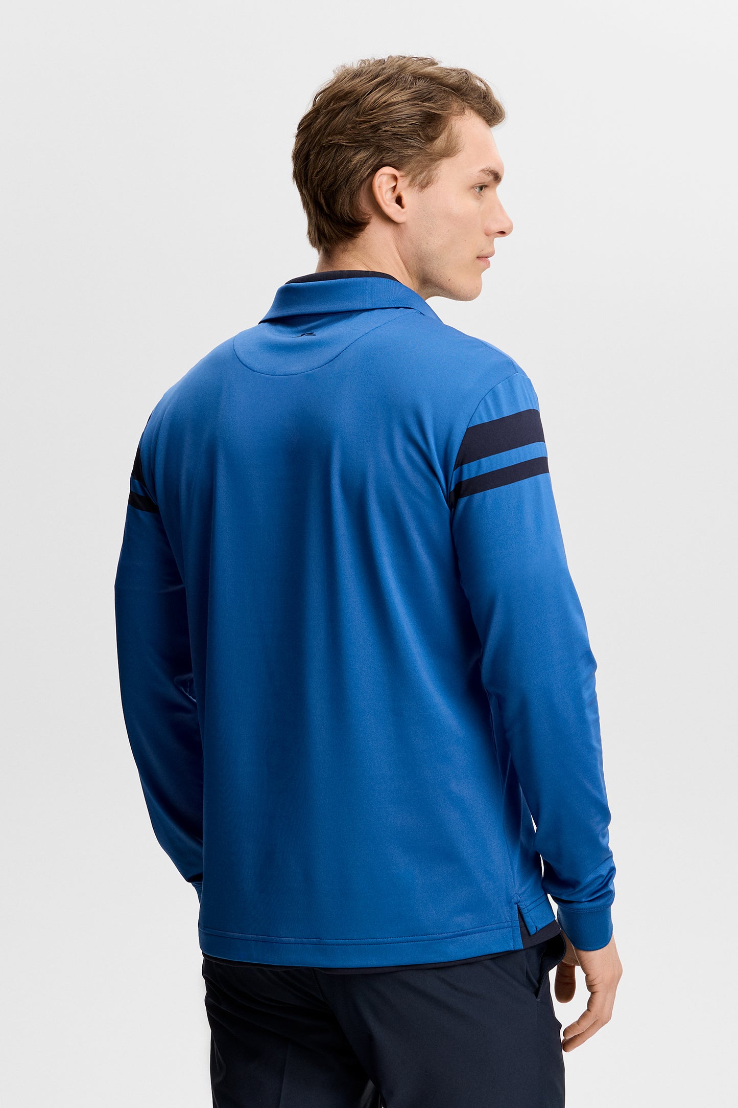 Set bagfra: Blå Kenny LS stripe polo med mørke ærmestriber og et lille Bridge-logo.