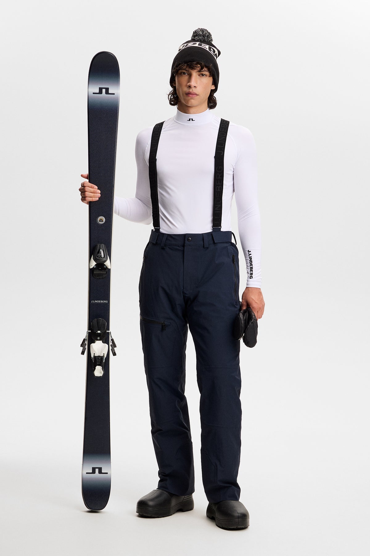 Vorderansicht: Crue Suspender Pant in JL Navy mit schwarzen Hosenträgern, getragen an einem Model mit Ski.