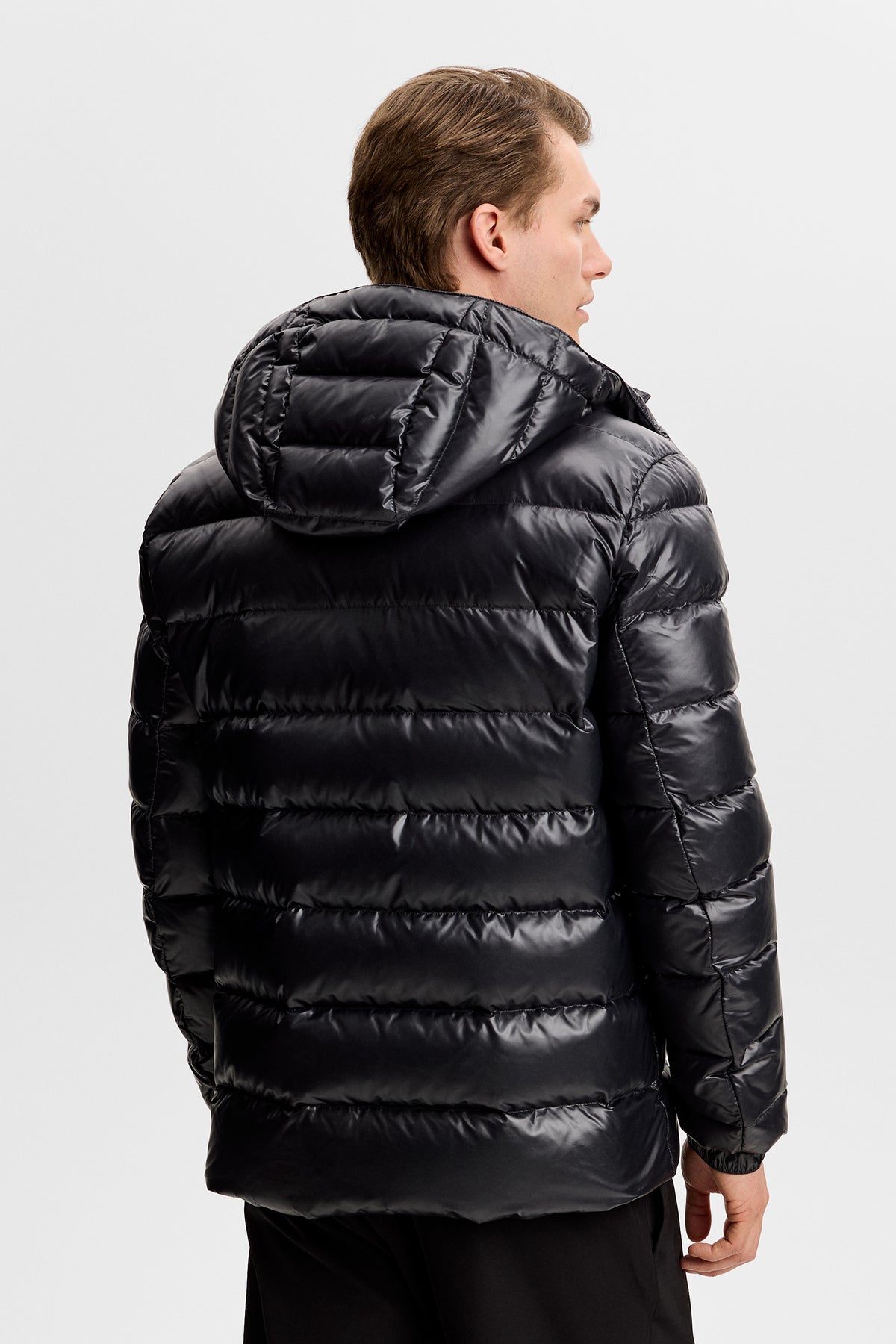 Rückansicht: Schwarze Creek Light Down Jacket mit glänzender Steppung und Kapuze an einem Model.