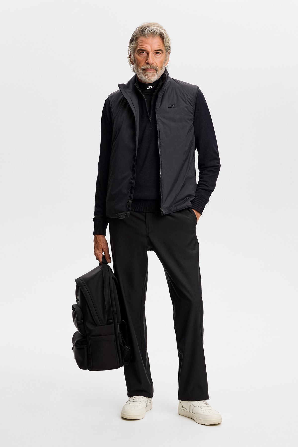 Forfra: Sort Jeffrey Windbreaker Sweater stylet under en sort vest med sorte bukser og rygsæk.