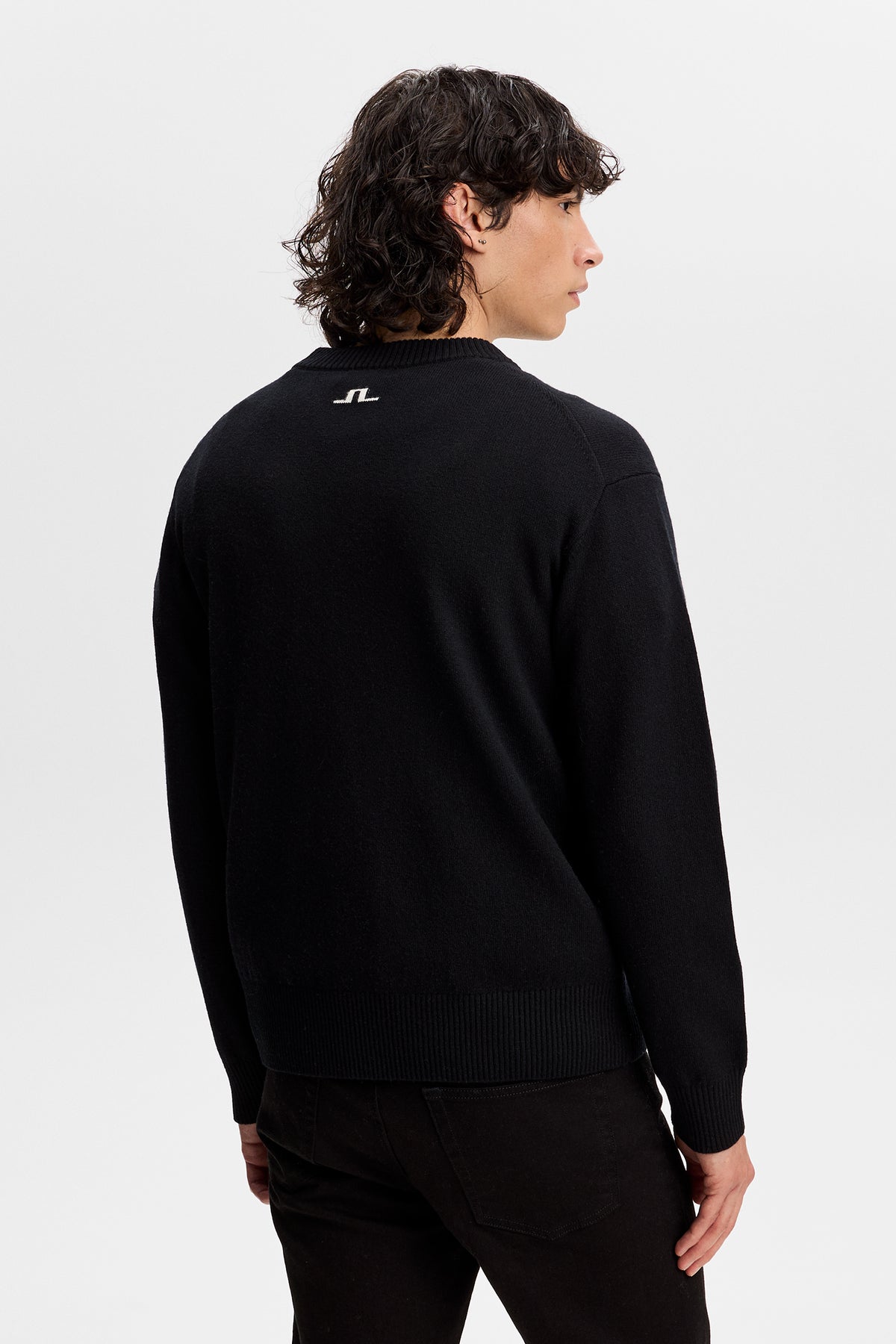 Set bagfra: Sort William Knitted Sweater med rund hals, ribstrikkede kanter og hvidt Bridge-logo øverst på ryggen.