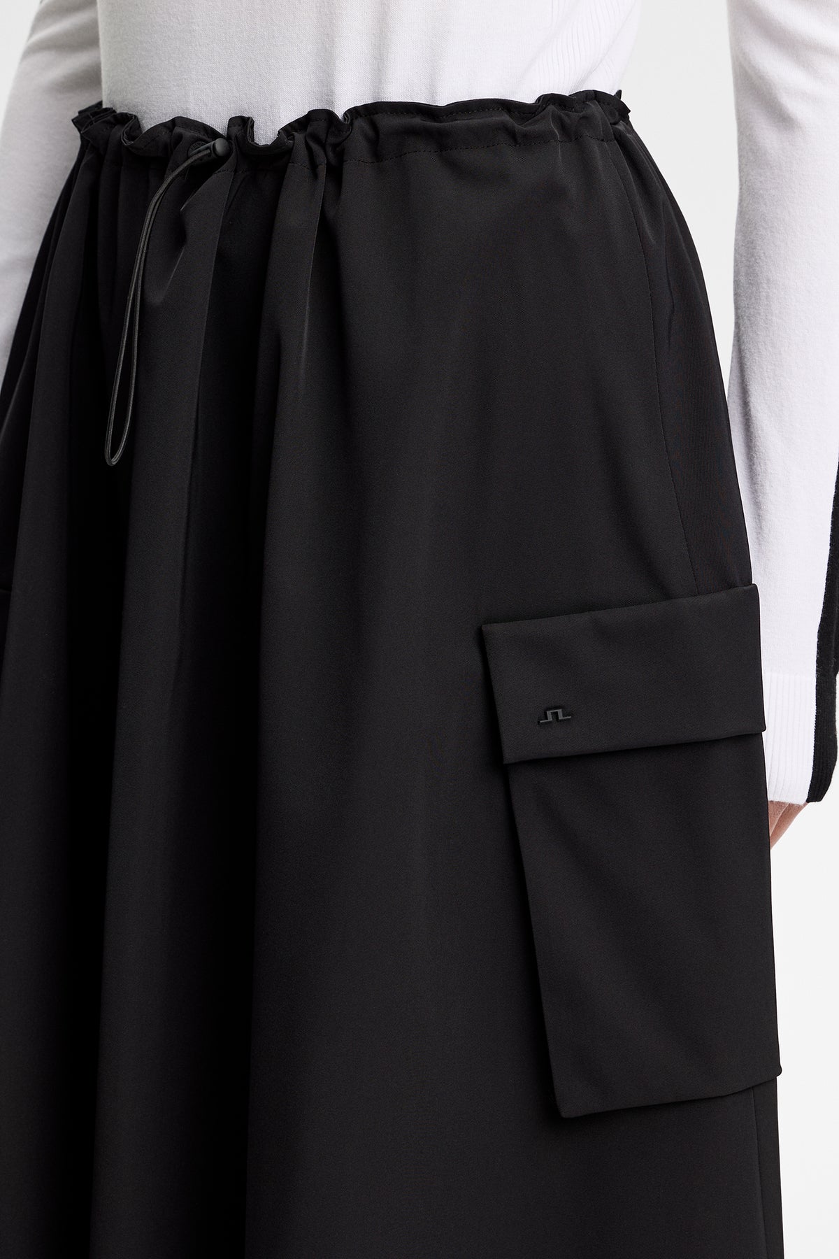 Gros plan : Essa Tech Drape Skirt noire avec taille à cordon de serrage et poche à rabat avec logo Bridge.