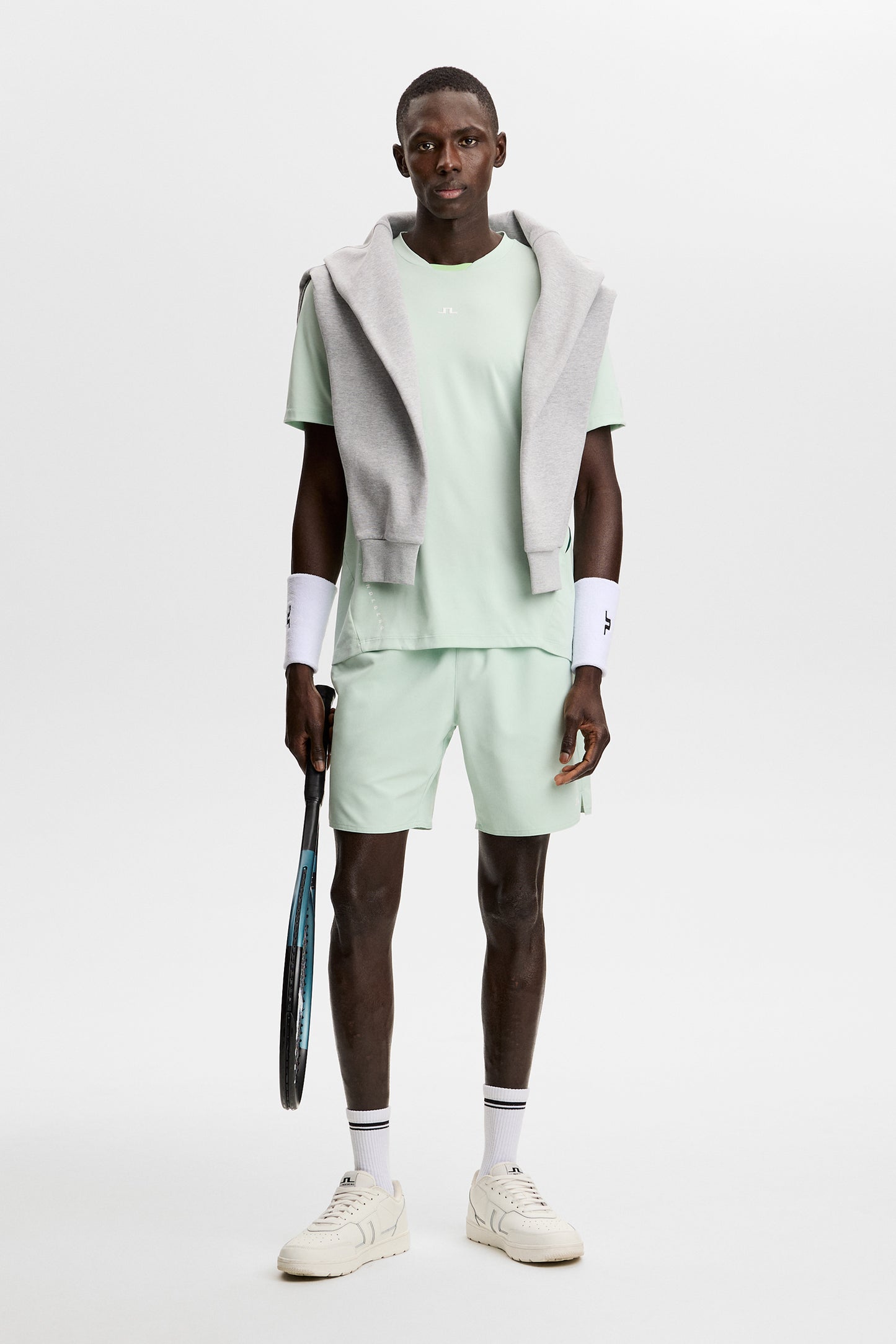 Model wearing the light green Dennis T-shirt with matching shorts and a tennis racket in a studio setting.