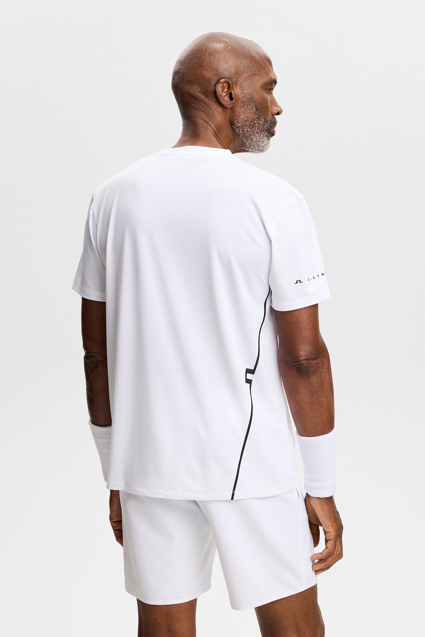 Achteraanzicht: Model draagt het witte Leroy T-shirt met zwarte streep aan de zijkant en logo op de mouw.