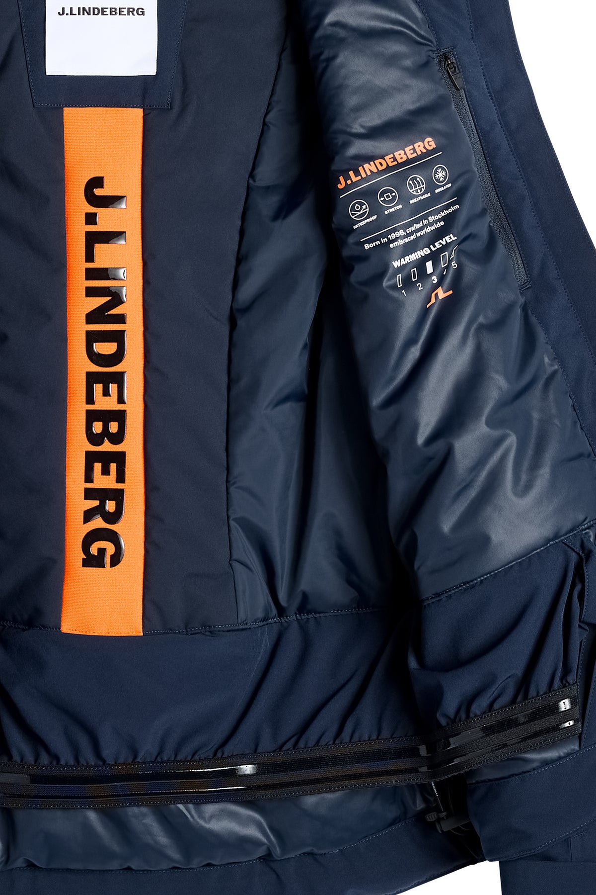 Detailansicht: Lilia Jacket in JL Navy mit orangem J.LINDEBERG-Logo, Innentasche und Schneefang.