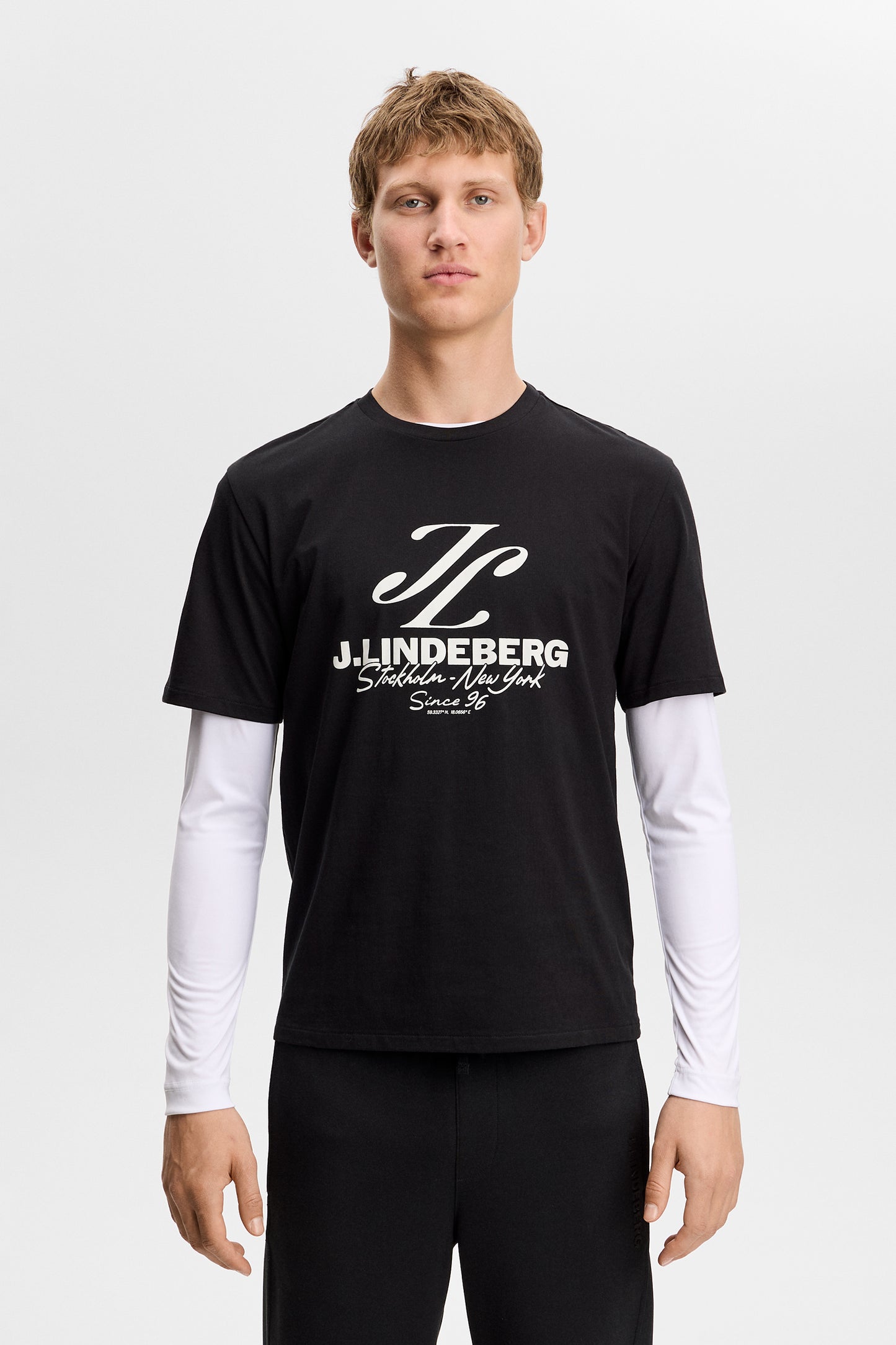 Model wearing the black Alpha Graphic T-shirt with white chest graphic, layered over a long-sleeve top.