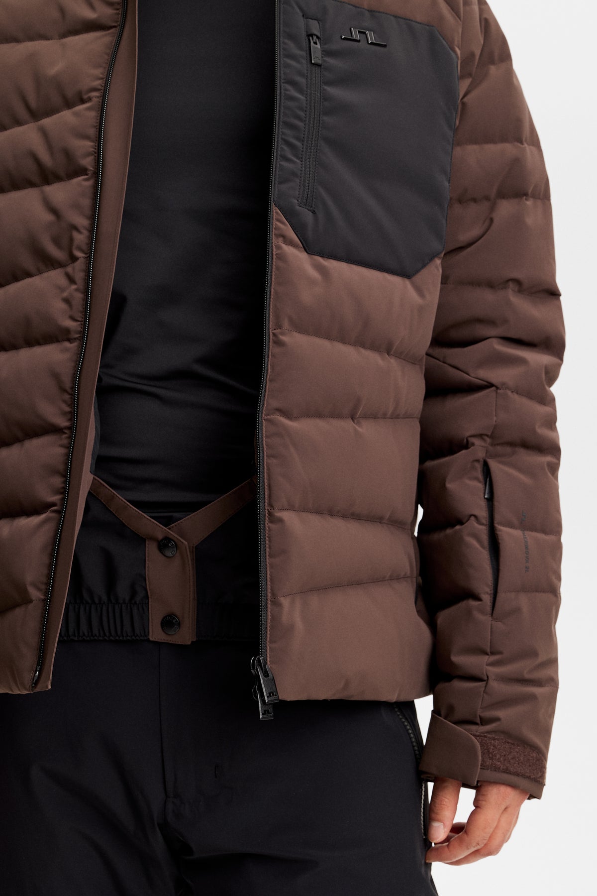 Close-up view of the Thornton Down Jacket in Seal Brown with chest pocket, Bridge logo, and snow gaiter.