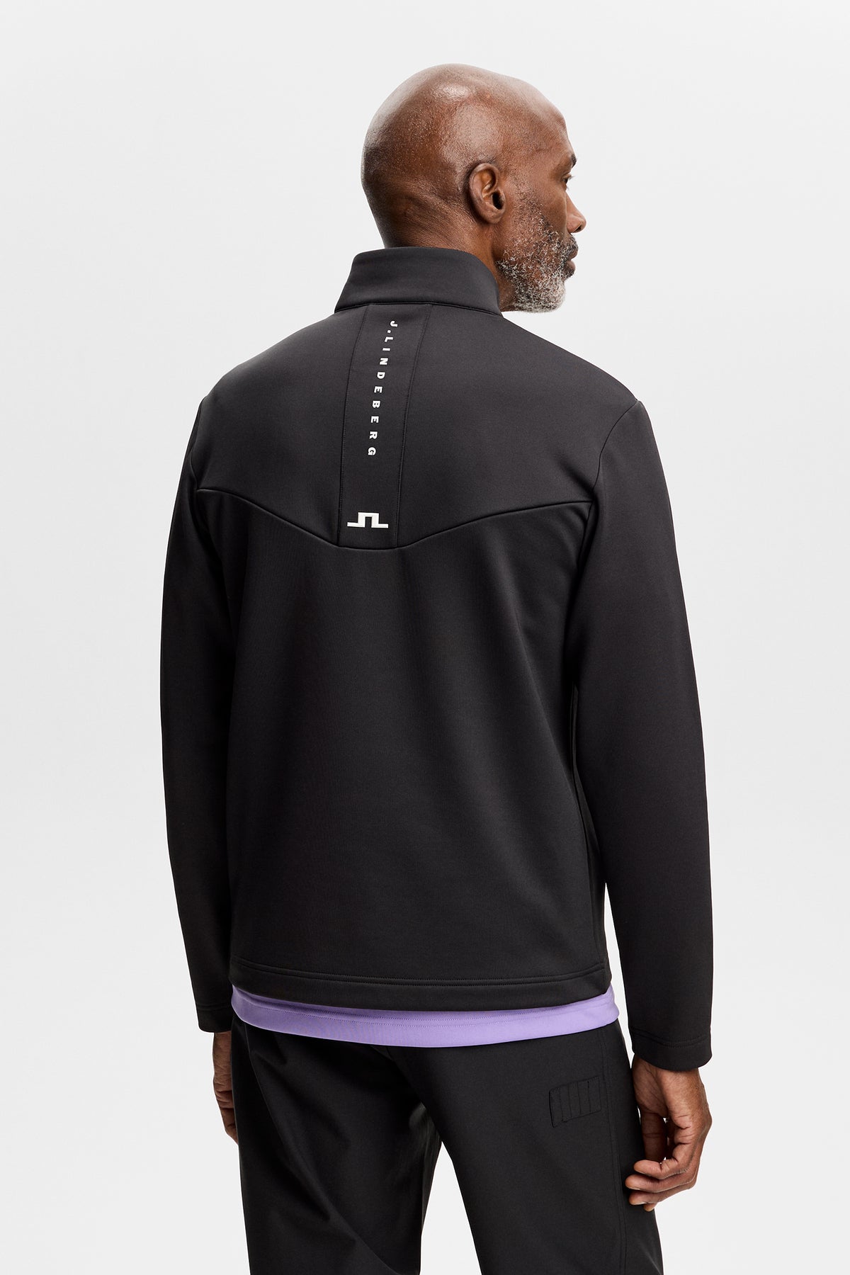 Bakifrån: Modell bär Maclean Quarter Zip Mid Layer i Black med vertikal J.Lindeberg-text och Bridge-logotyp på ryggen.