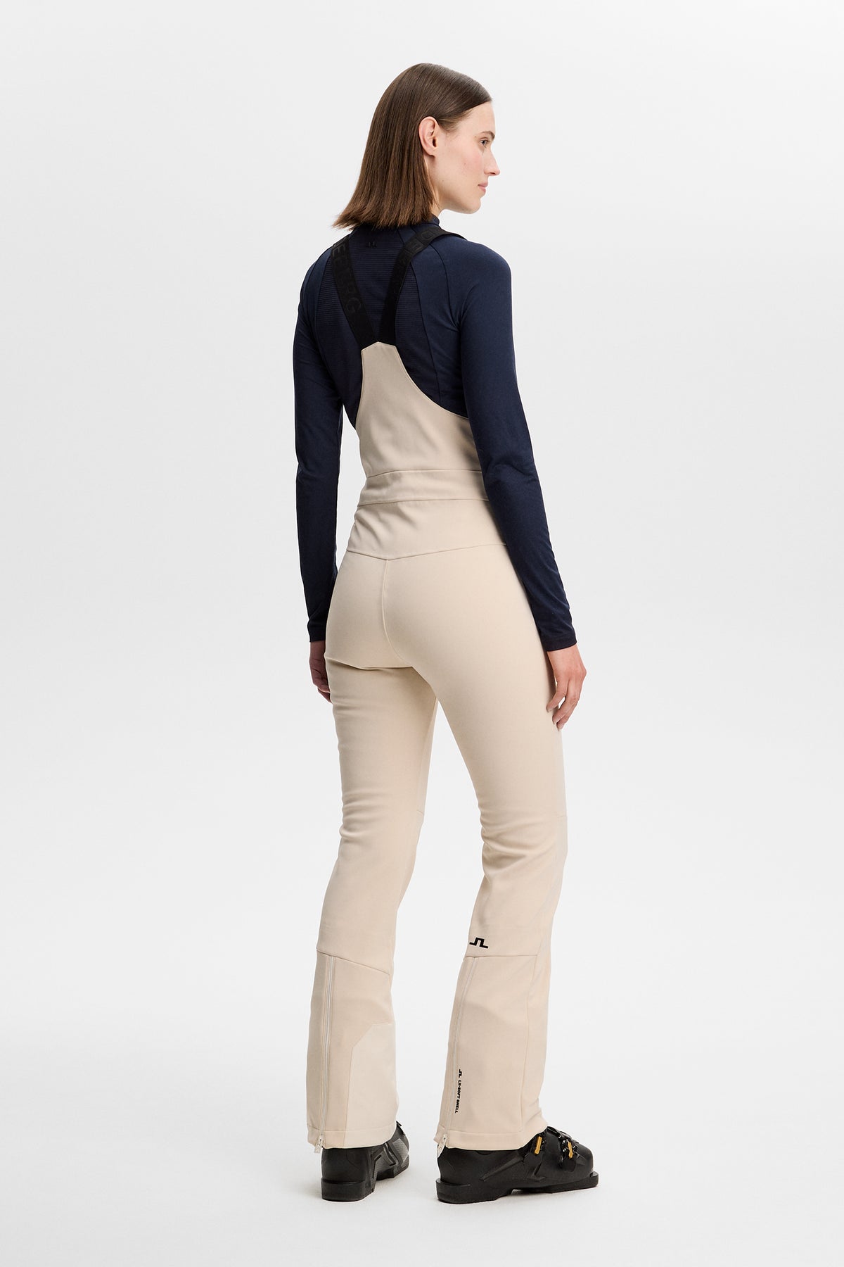 Achteraanzicht: Model draagt de Aviana Softshell Bib Pant in Moonbeam met zwarte bretels en Bridge-logo op het been.