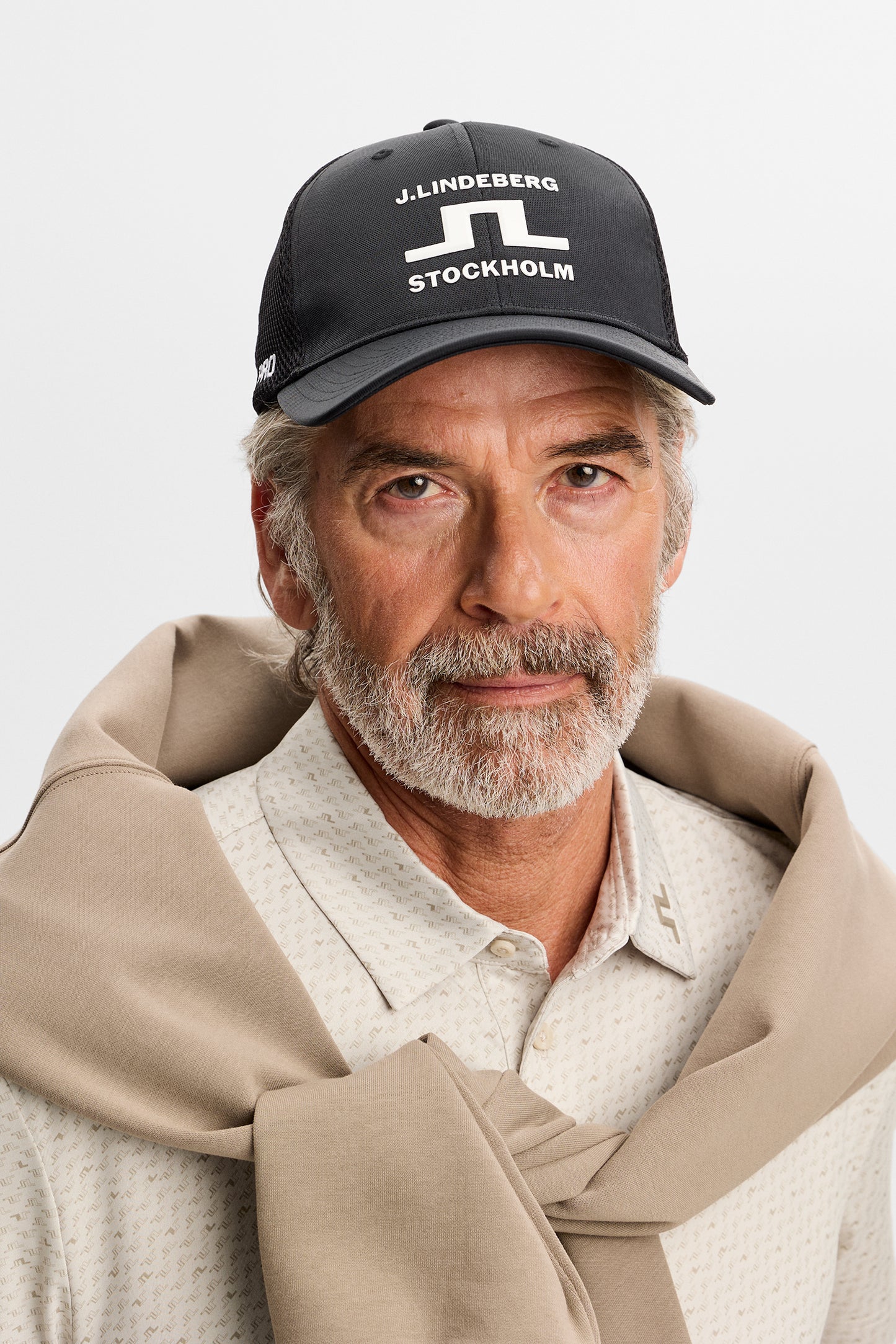 Sett forfra: Svart JL Pro Cap med hvit J.Lindeberg Stockholm-grafikk foran, på modell i studio.