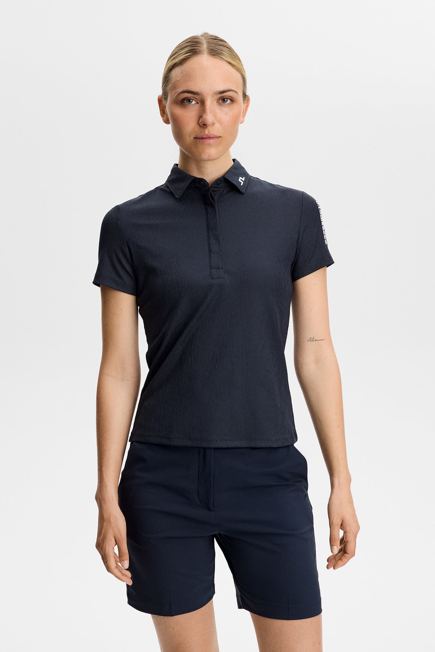 Vorderansicht: Tour Tech Textured Polo in JL Navy mit weißem Bridge-Logo am Kragen, getragen zu Shorts.