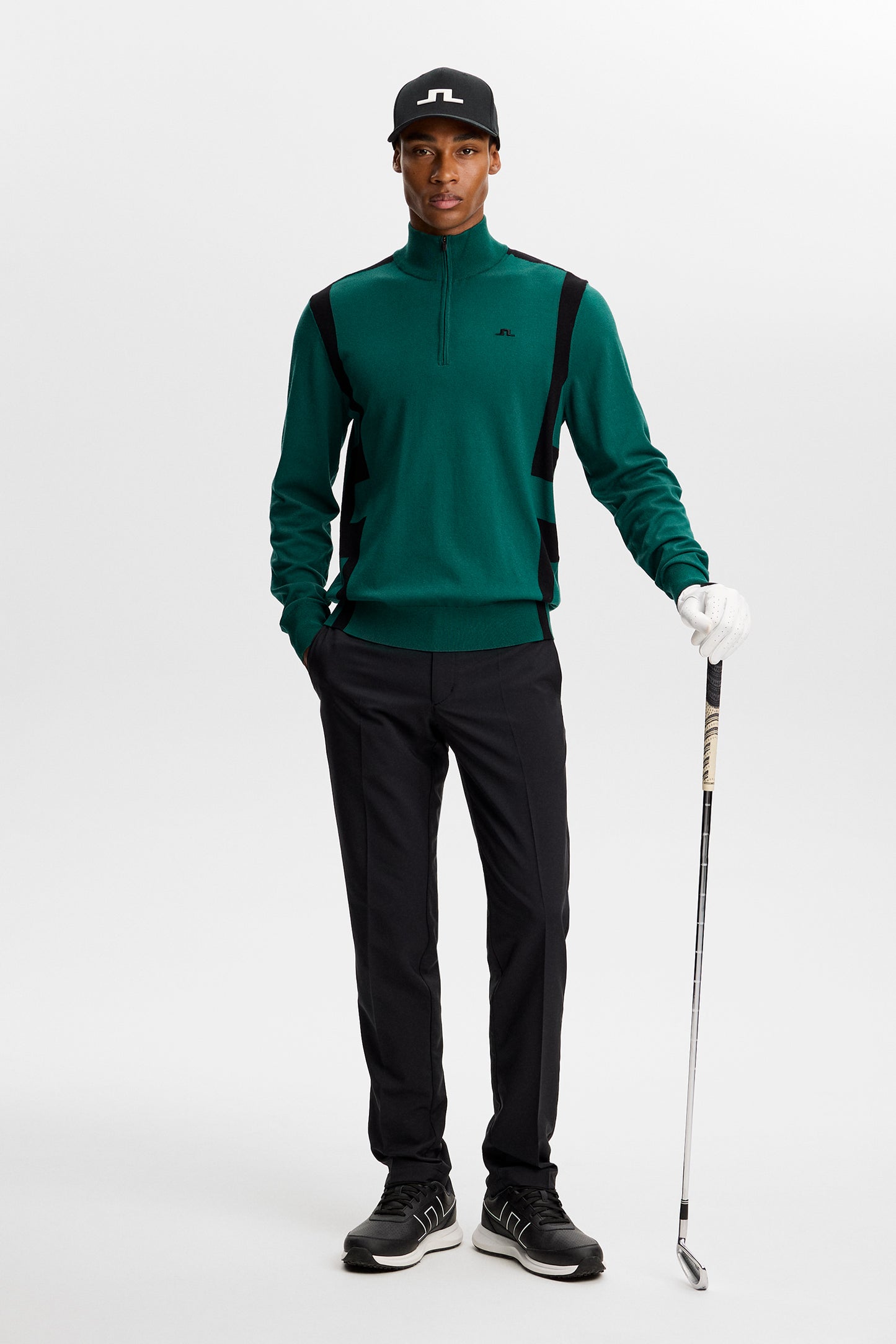 Front view: Model iført Kendrick Knitted Zip Sweater i grøn med sorte sidepaneler, halv lynlås og lille Bridge-logo i et studie.