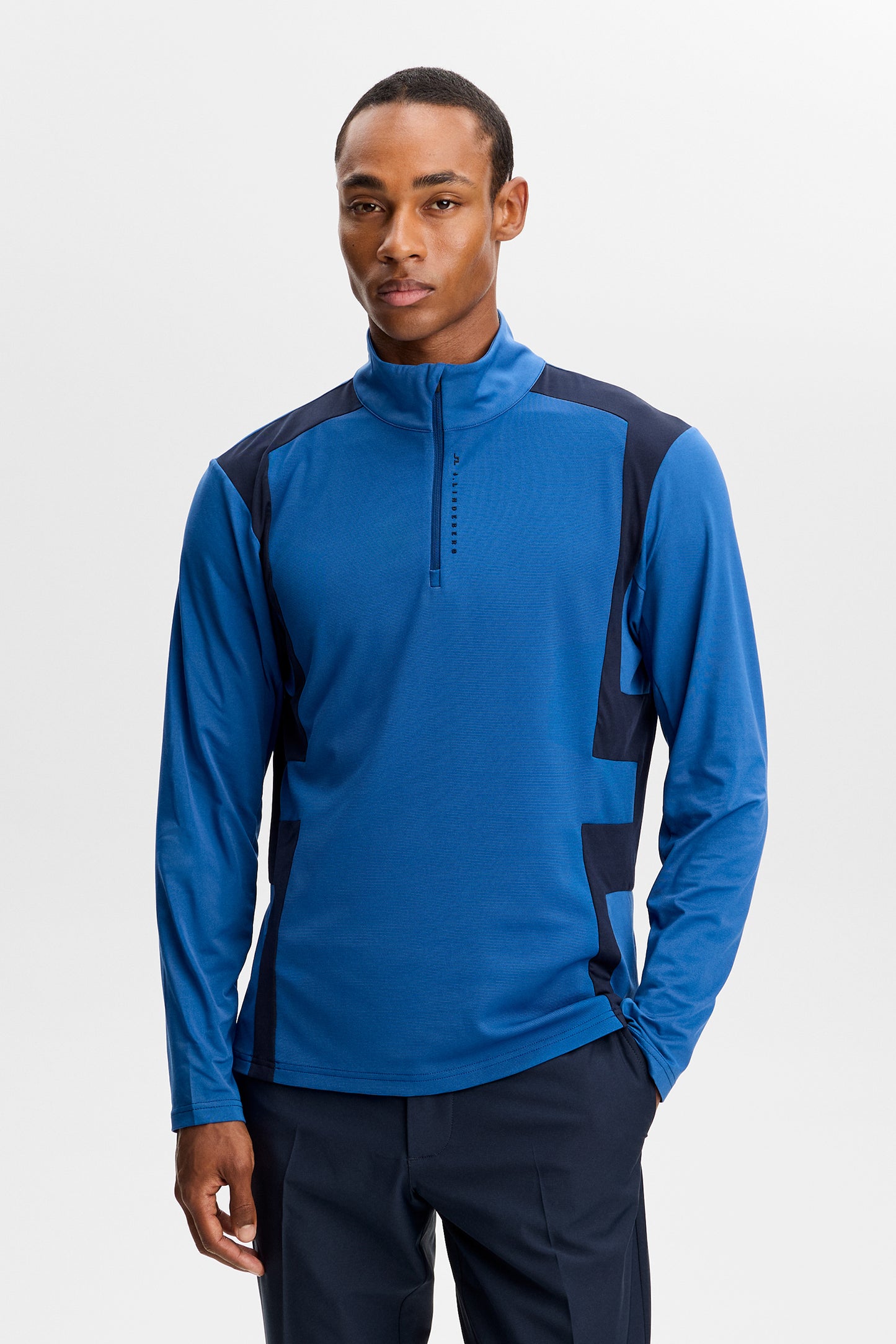 Vooraanzicht: Model draagt de blauwe Finn Quarter Zip Mid Layer in Set Sail met contrasterende panelen en korte rits.