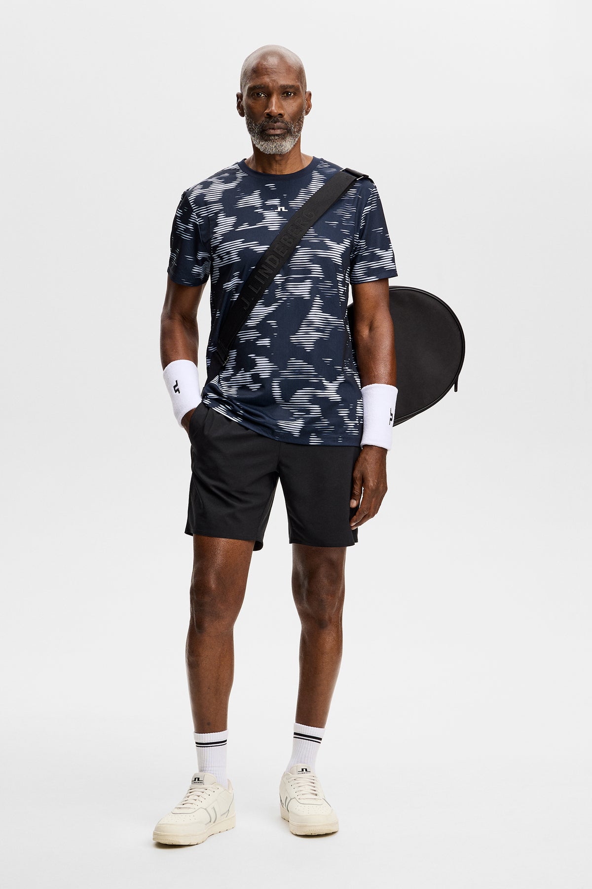 Vooraanzicht: Model draagt het Josip Printed T-shirt met all-over print, een zwarte short en tennistas.