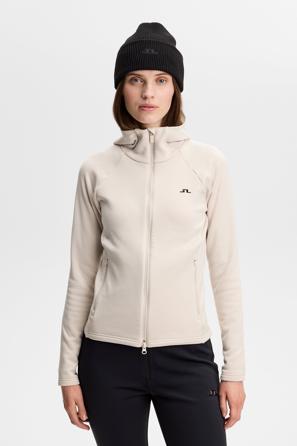 Front view: Model wearing the Portia Polartec Hood in Moonbeam with a two-way zipper and Bridge logo.