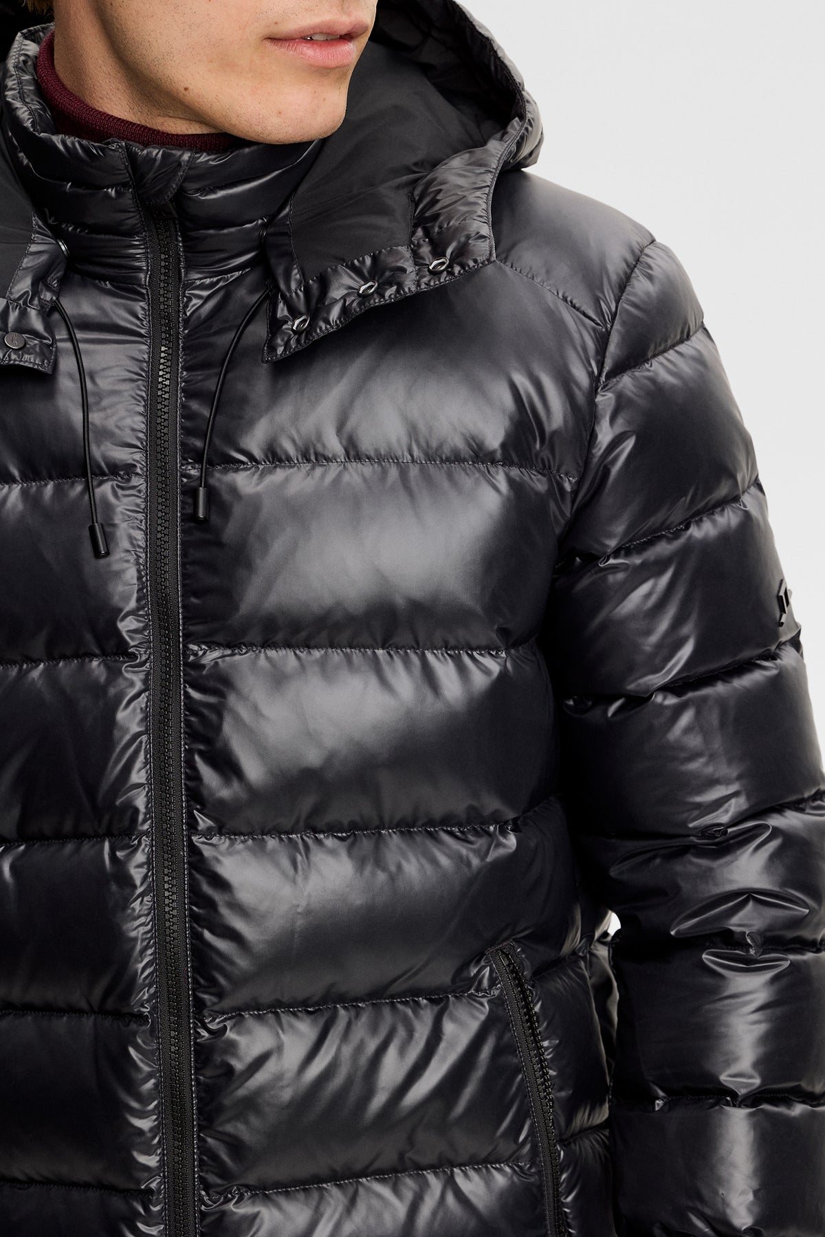 Detailansicht: Schwarze Creek Light Down Jacket mit glänzender Steppoptik, Reißverschluss und Kapuze mit Kordelzug.