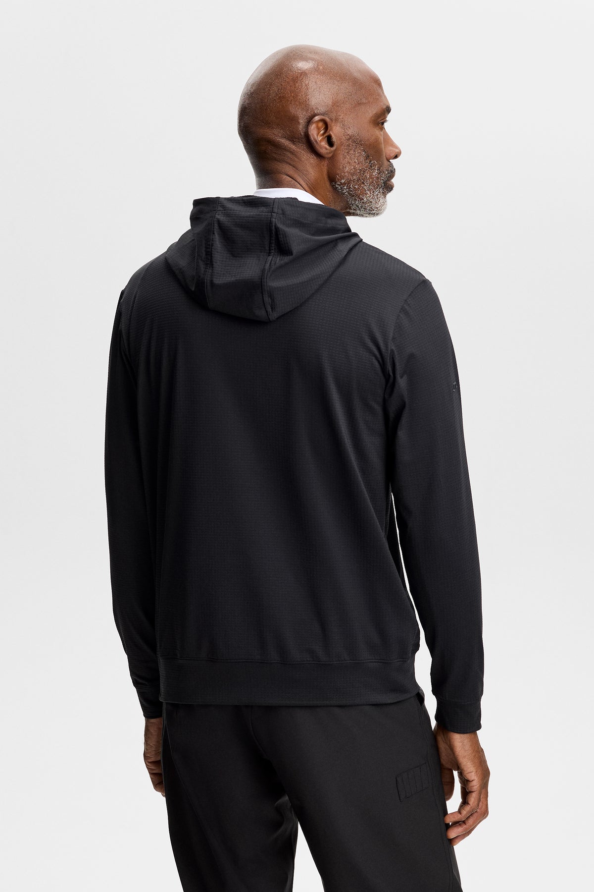 Set bagfra: Sort Vent Golf Hood med fast hætte og tekstureret overflade, båret med sorte bukser.