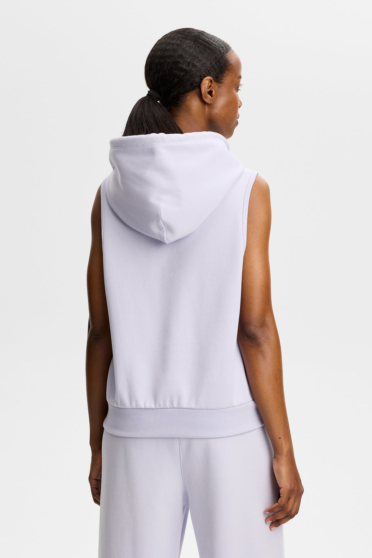 Rückansicht: Sarah Sleeveless Hood in Helllila an einem Model mit Kapuze und geripptem Saum.
