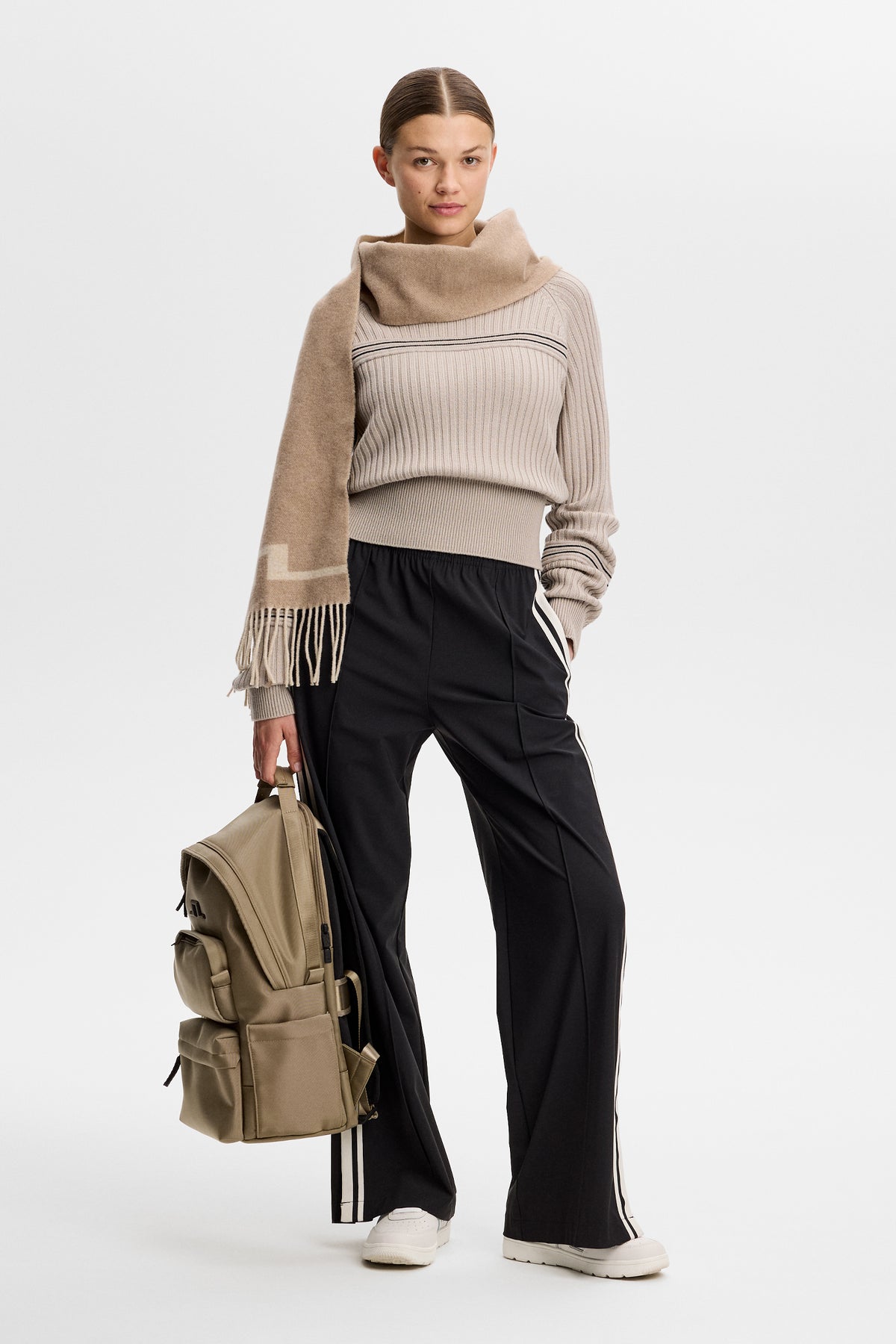Vorderansicht: Hilda Knitted Rib Hoodie in Moonbeam an einem Model mit beigem Schal, schwarzer Hose und Rucksack.