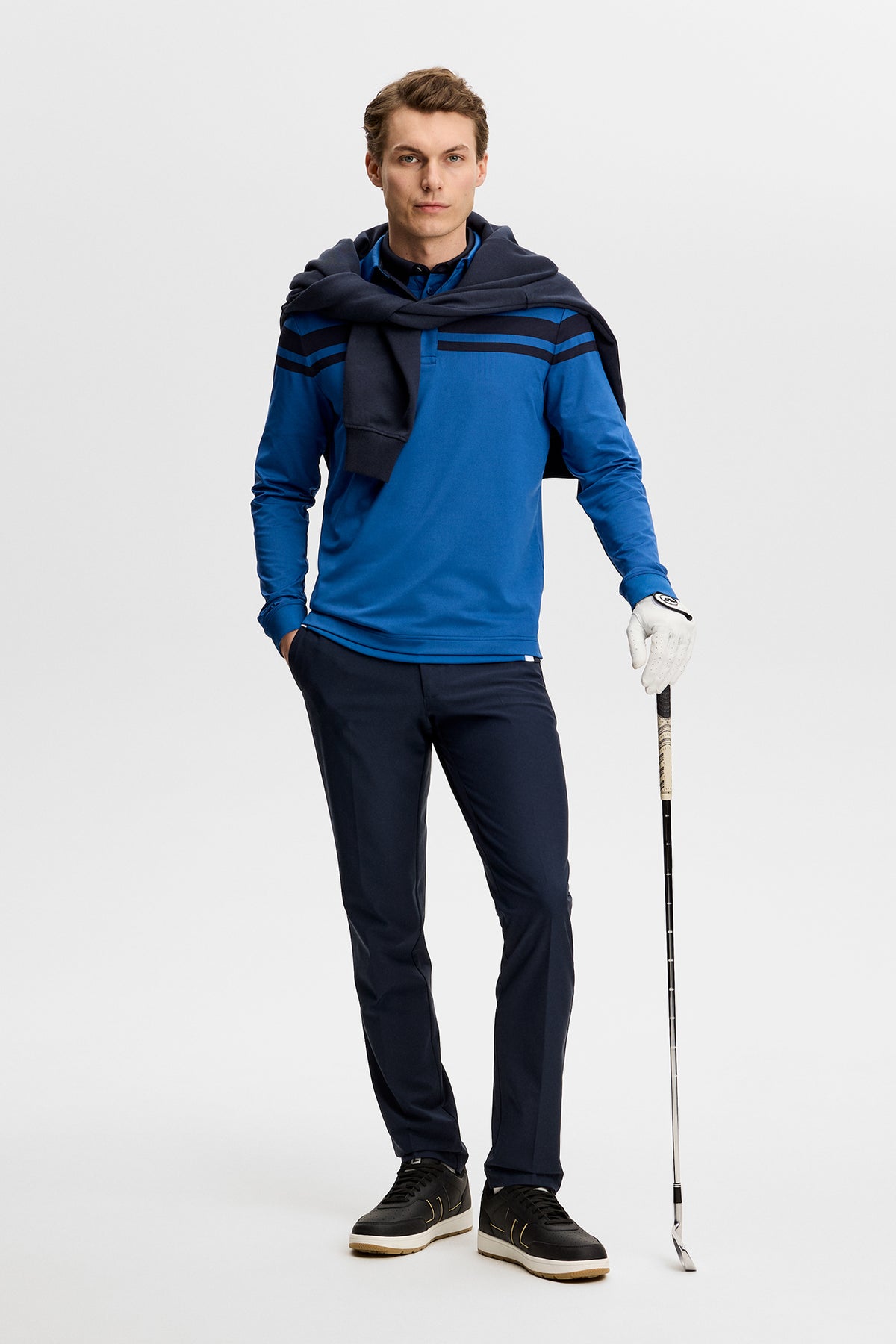 Set forfra: Blå Kenny LS stripe polo på en model, der holder en golfkølle i et studie.